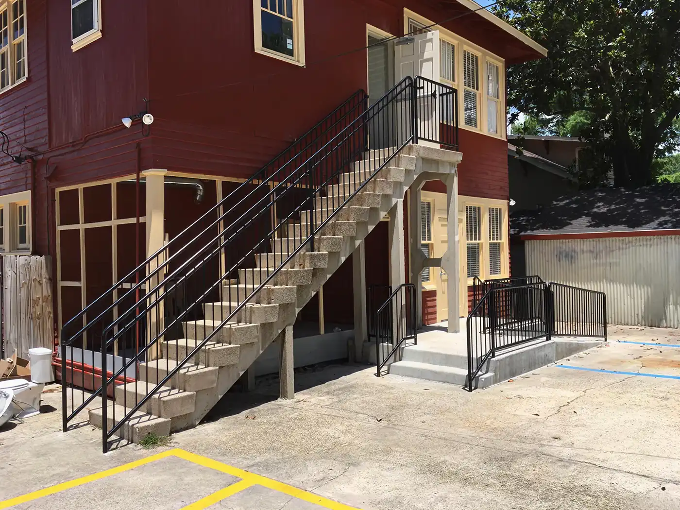Red two-story building with yellow trim, exterior stairs, wheelchair ramp, and concrete parking area.