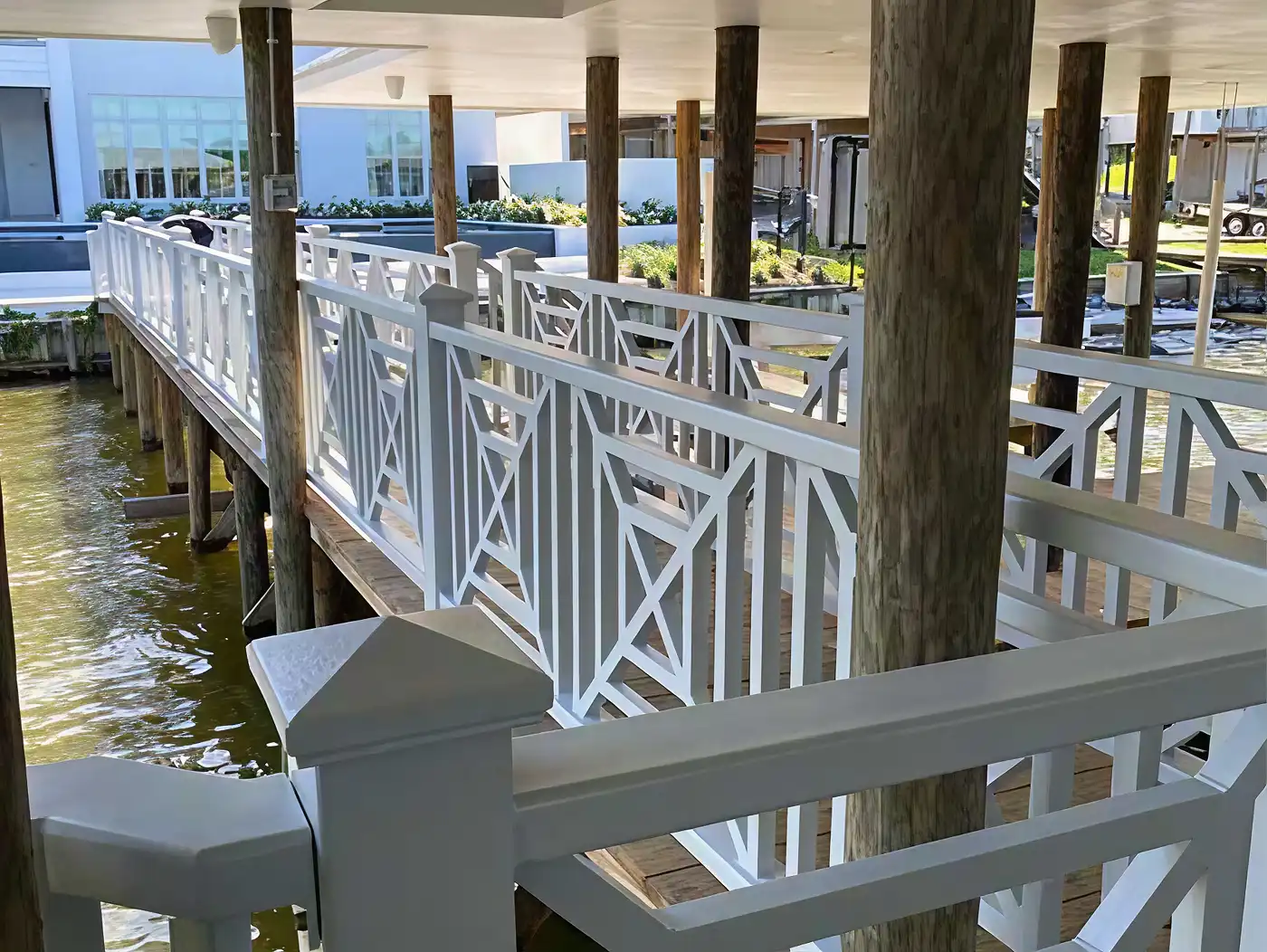 White wooden railing bridge over calm water supported by vertical wooden posts under a roof.