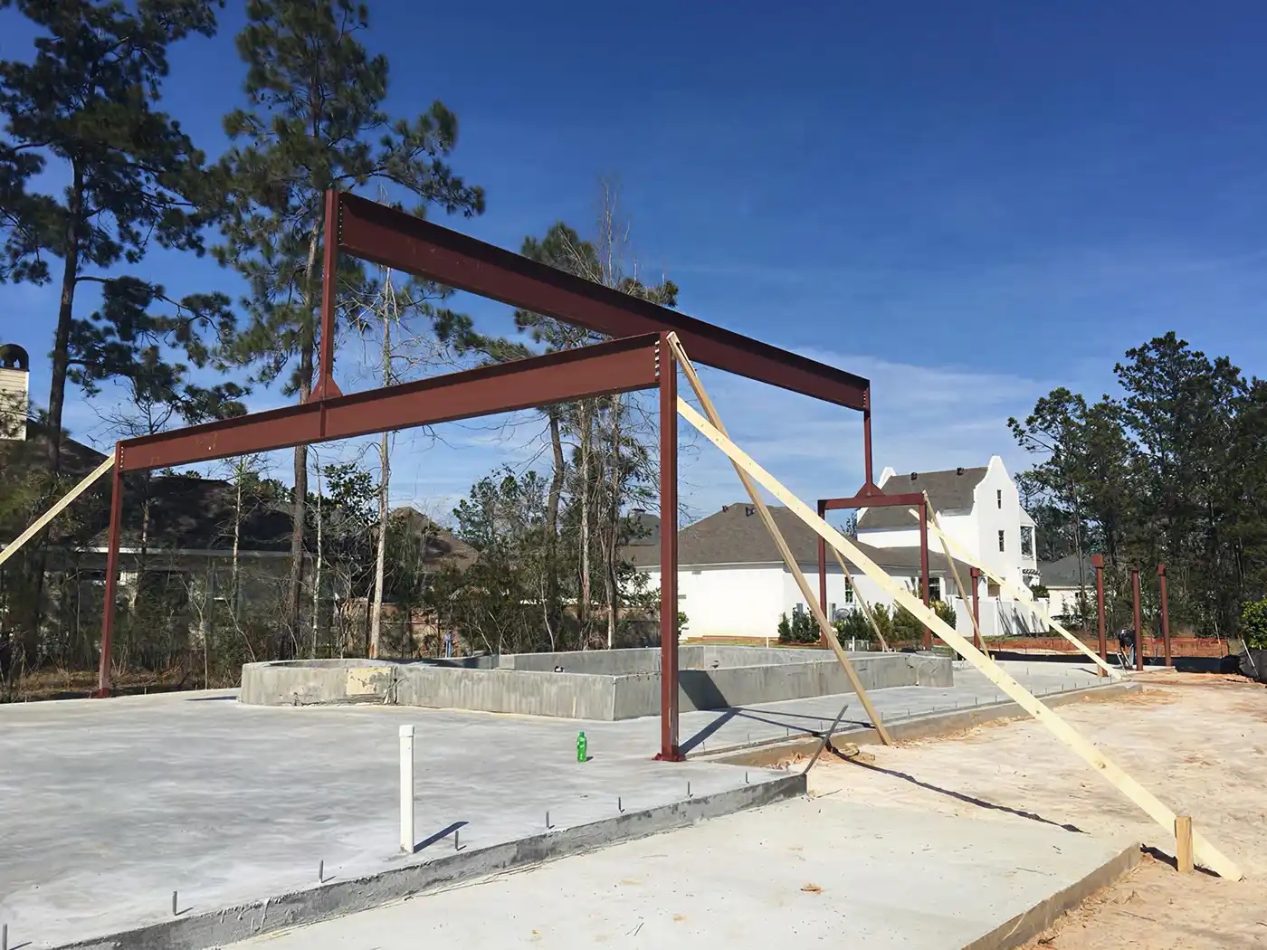 Steel framework with wooden braces on concrete foundation at a residential construction site.