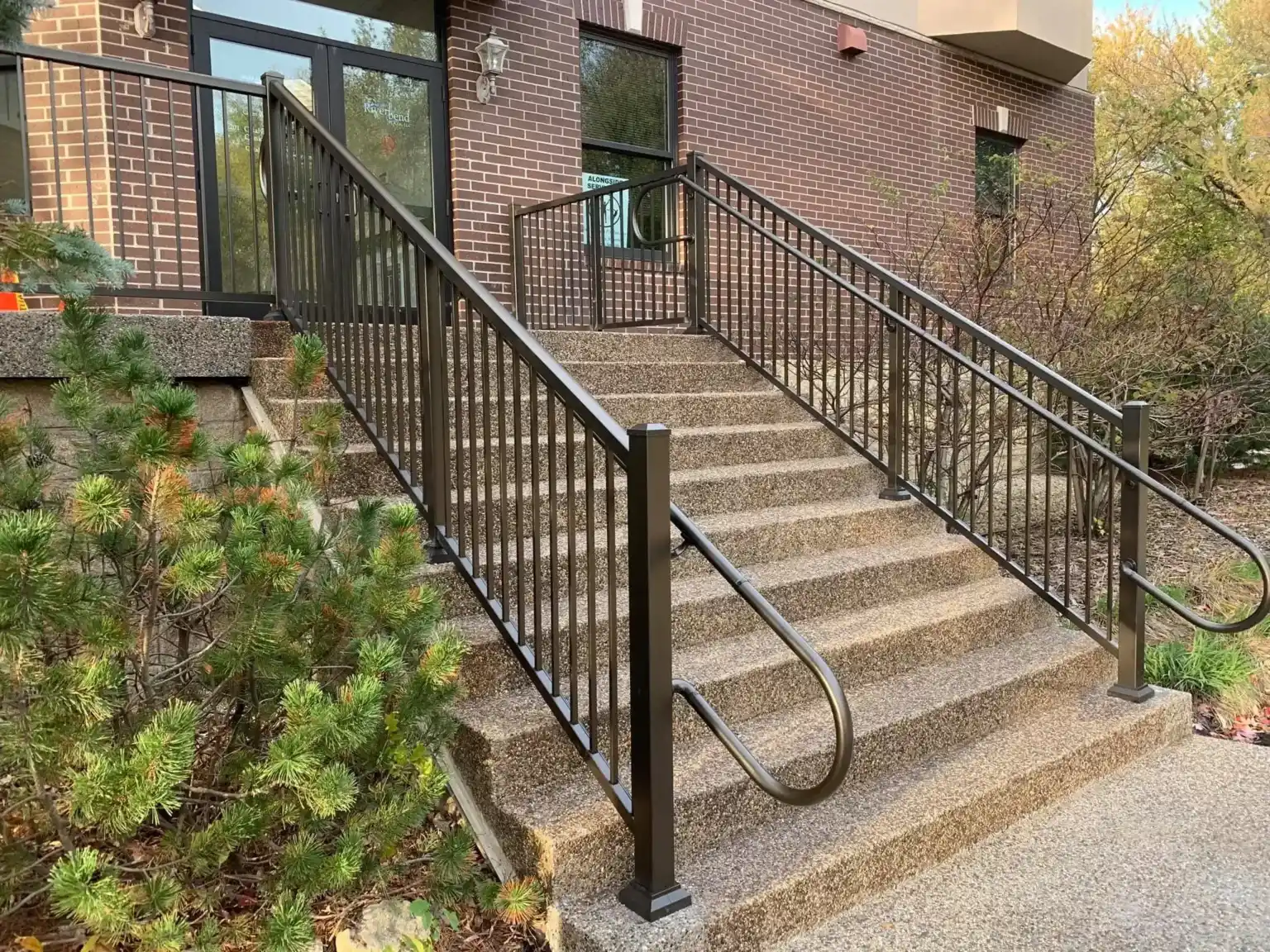 Stone staircase with metal railings leading to a glass door on a brick building.