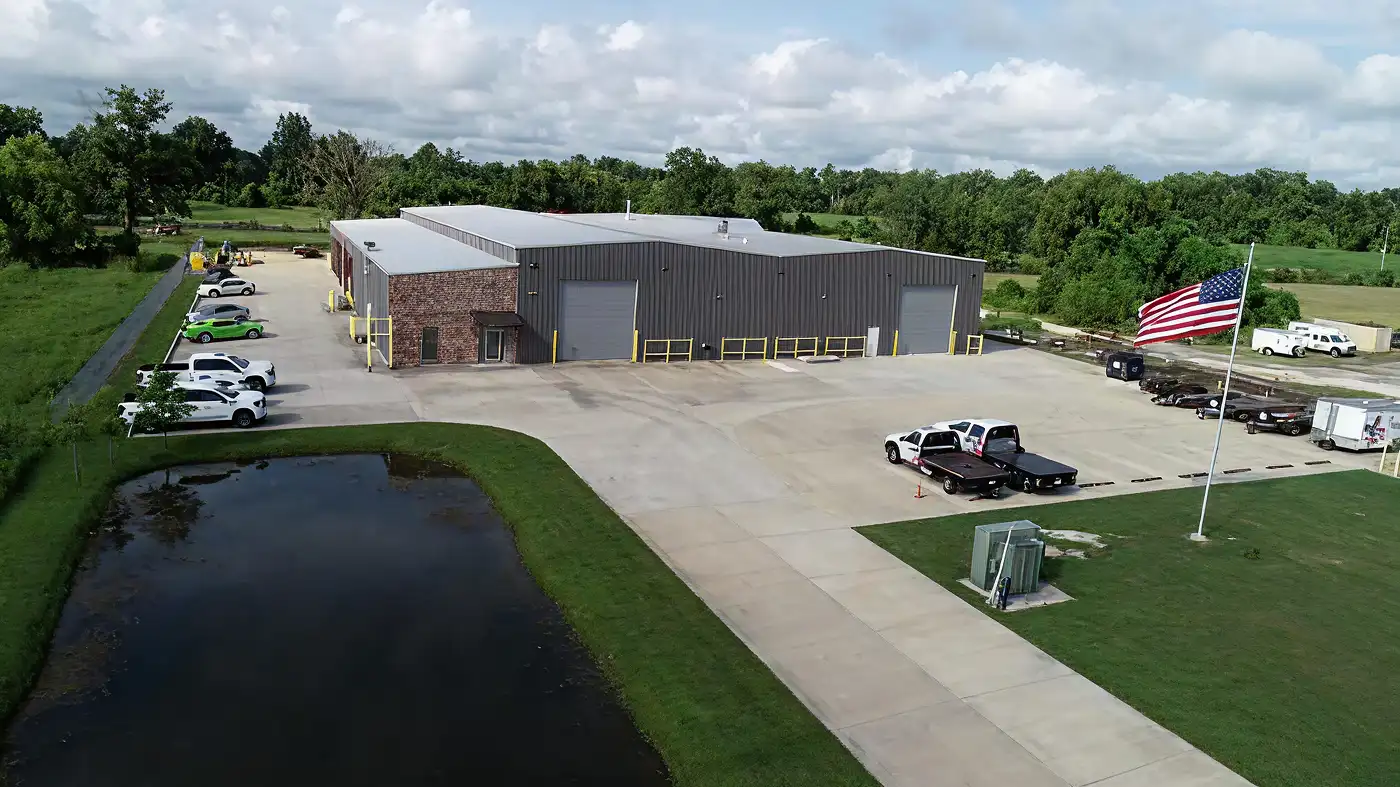 A commercial warehouse with metal siding and brick front, surrounded by parked vehicles and an American flag.