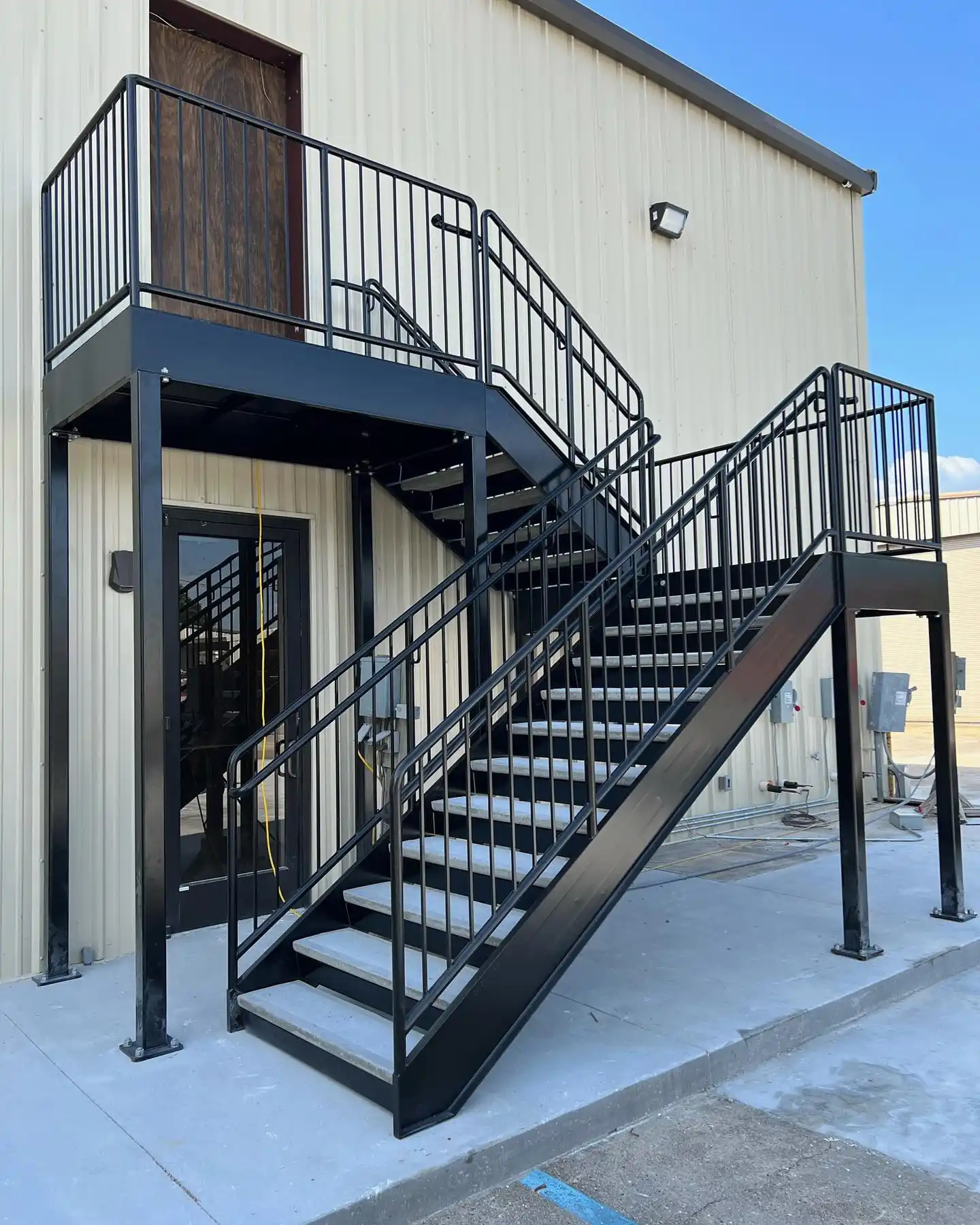 Black metal exterior stairs with railings leading to a second-floor door on a beige building.