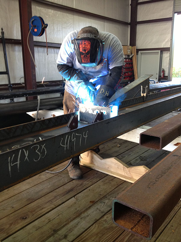 Worker welding steel beams inside a workshop with protective gear and sparks flying.