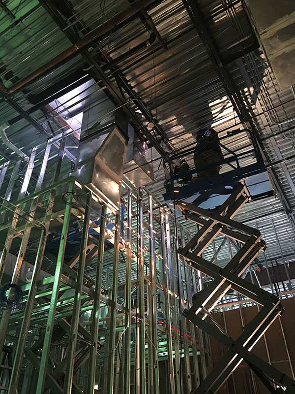 Worker on raised scissor lift inside building framing and exposed ceiling during construction.