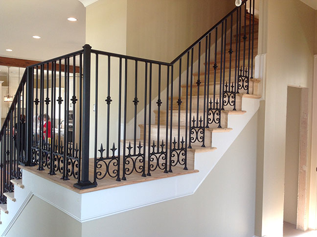 Interior staircase with light wood steps and decorative black wrought iron railings.