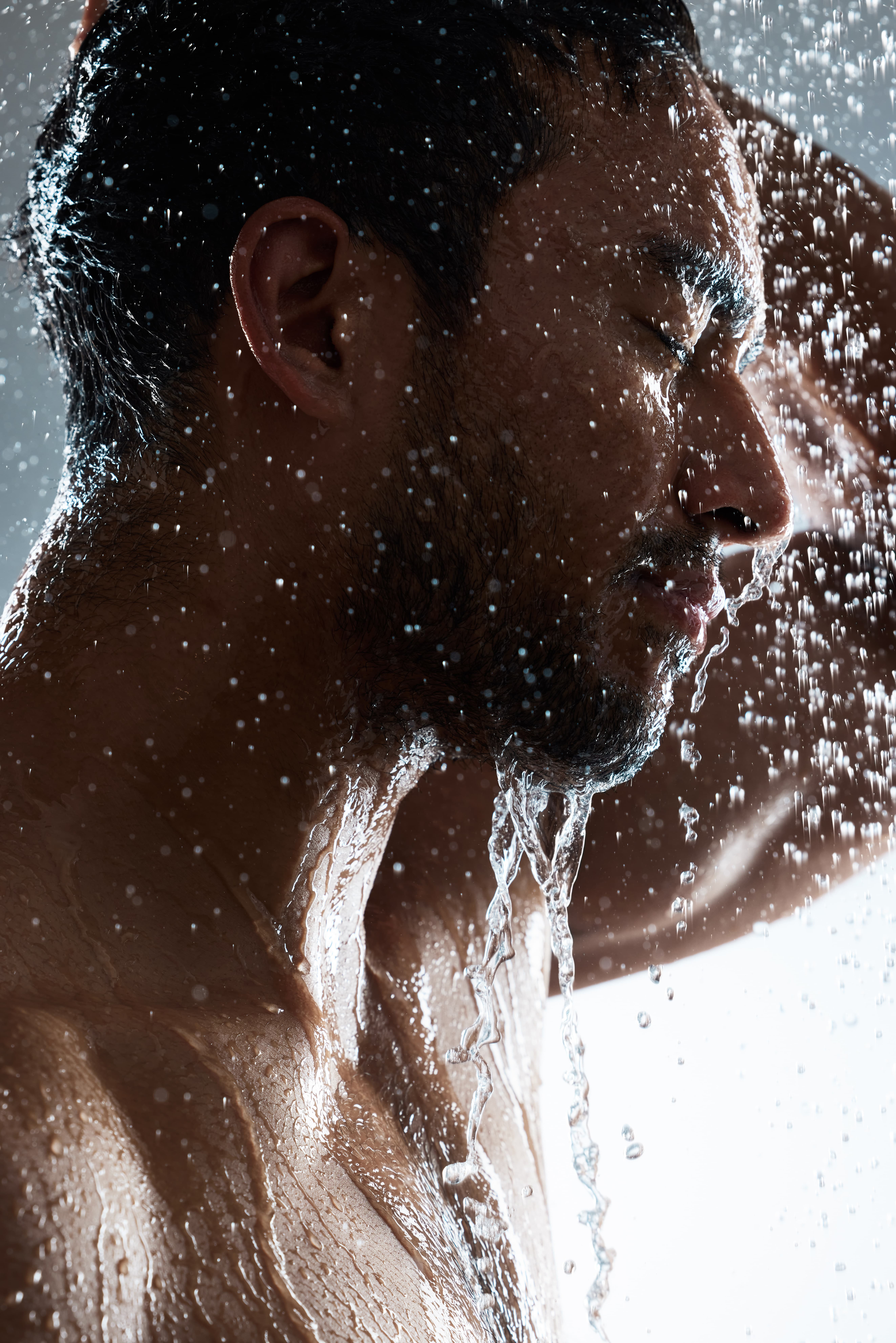 Close-up of a man with eyes closed enjoying water pouring over his face and body.