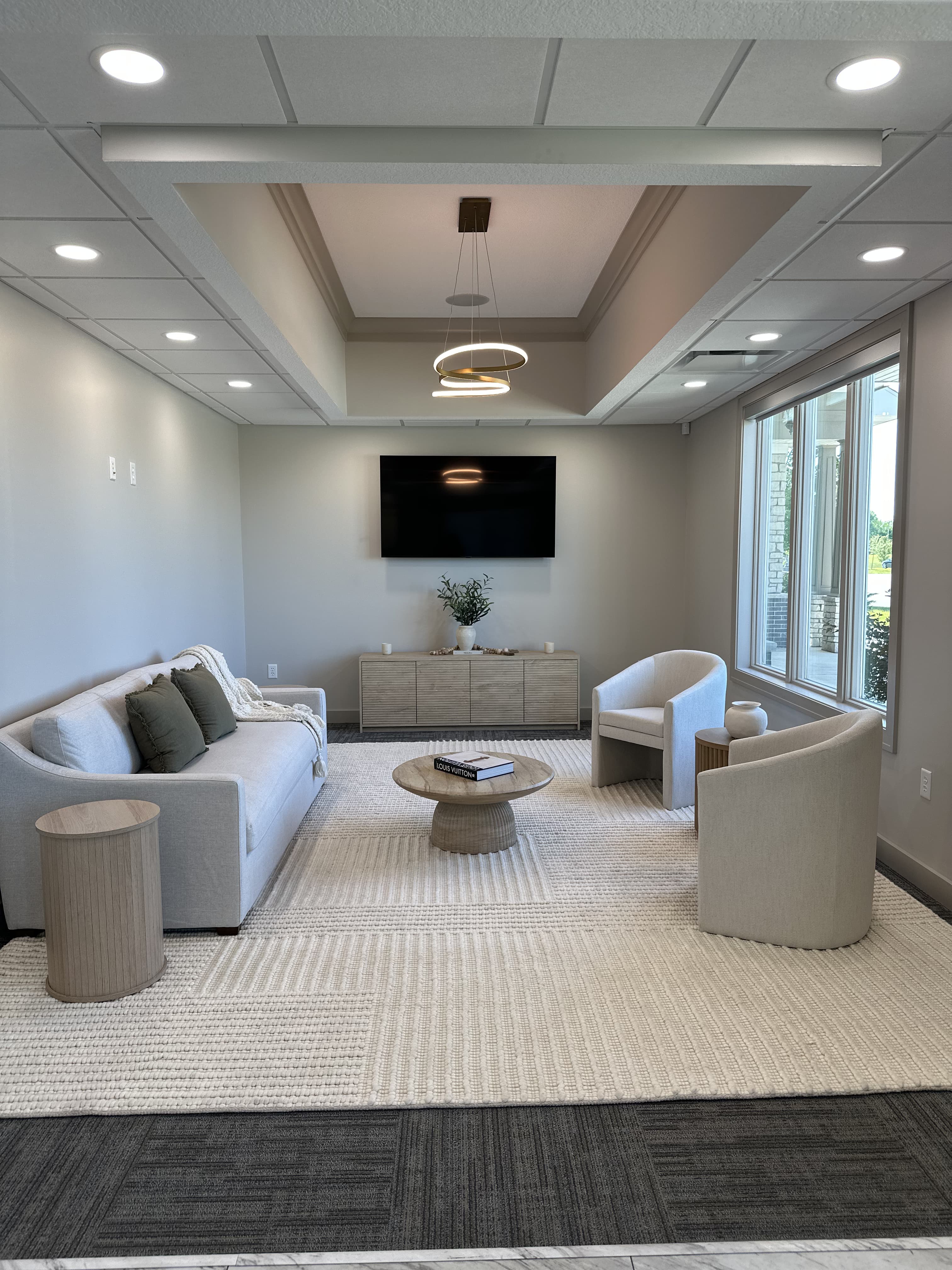 Modern living room with beige sofa, two chairs, round coffee table, and wall-mounted TV.