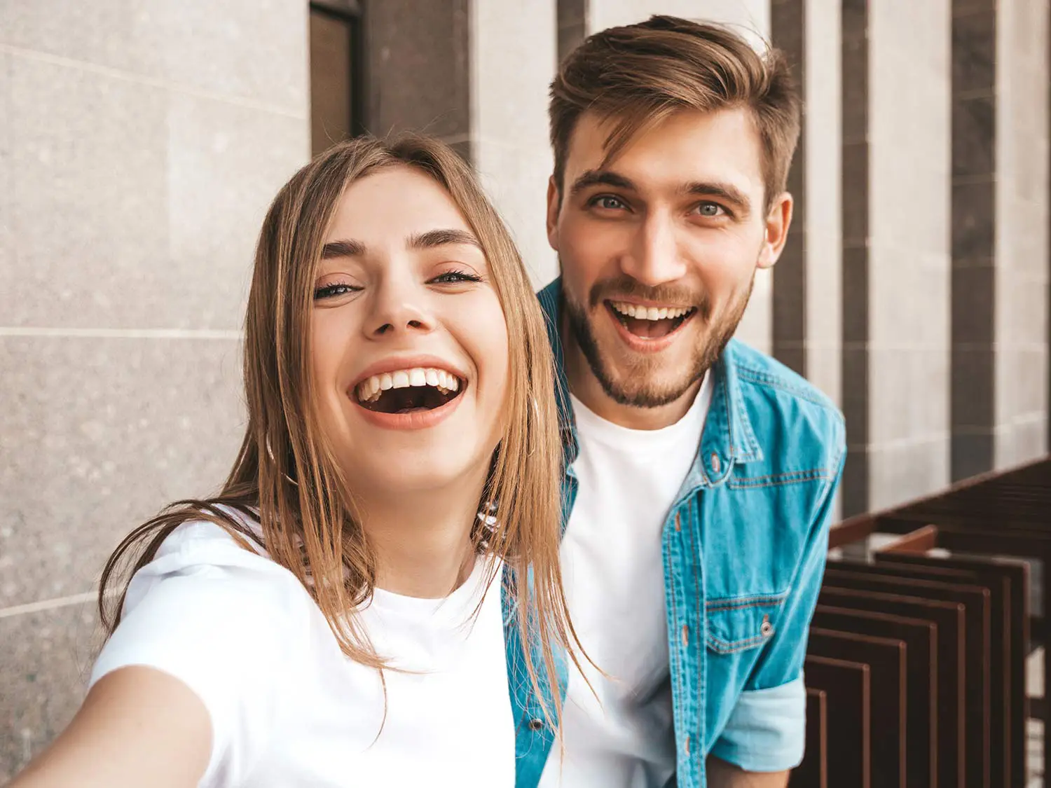 Smiling young woman and man taking a selfie outdoors in front of a stone wall.