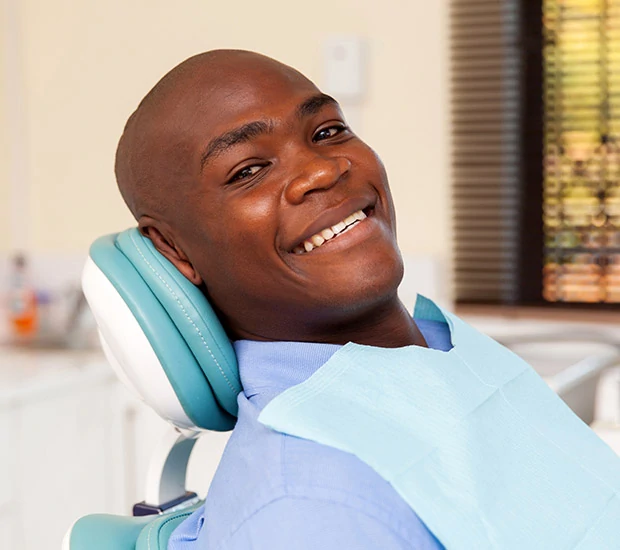 Smiling man sitting reclined in a dental chair wearing a light blue dental bib.