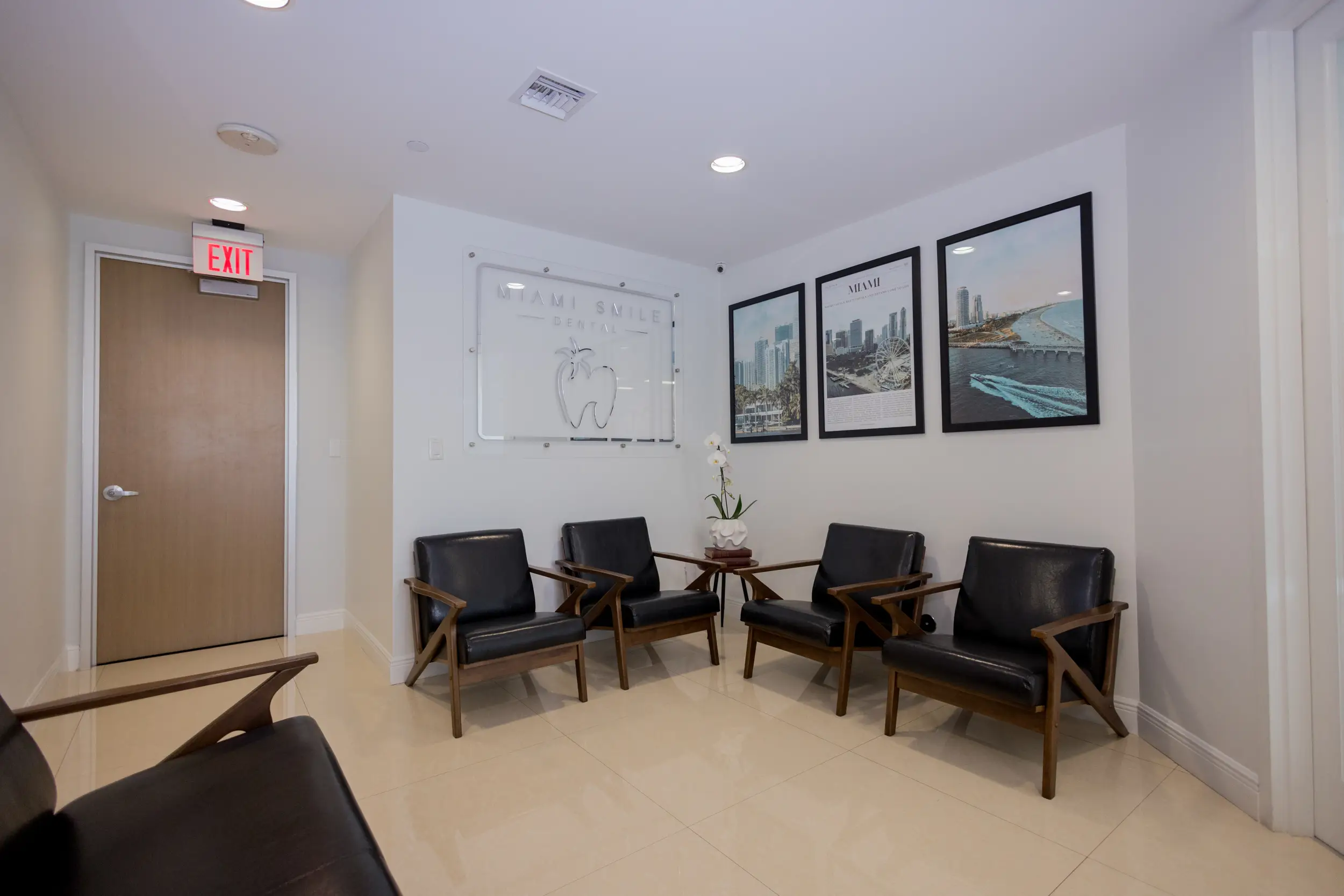 Waiting area with four black leather chairs, a small table with a white orchid, and framed photos of Miami on the wall.