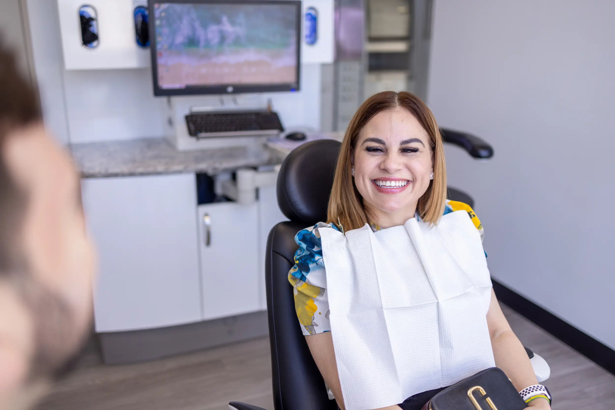 Smiling woman sitting in a dental chair wearing a dental bib in a clinic.