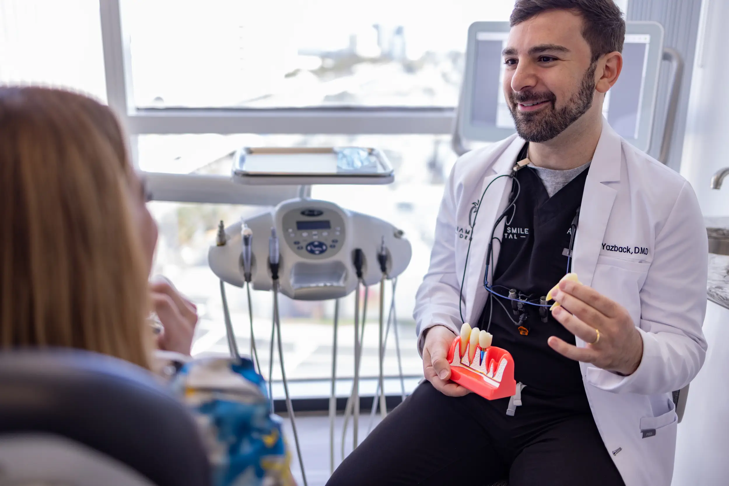 Dentist in a white coat explaining dental implants to a patient using a tooth model.