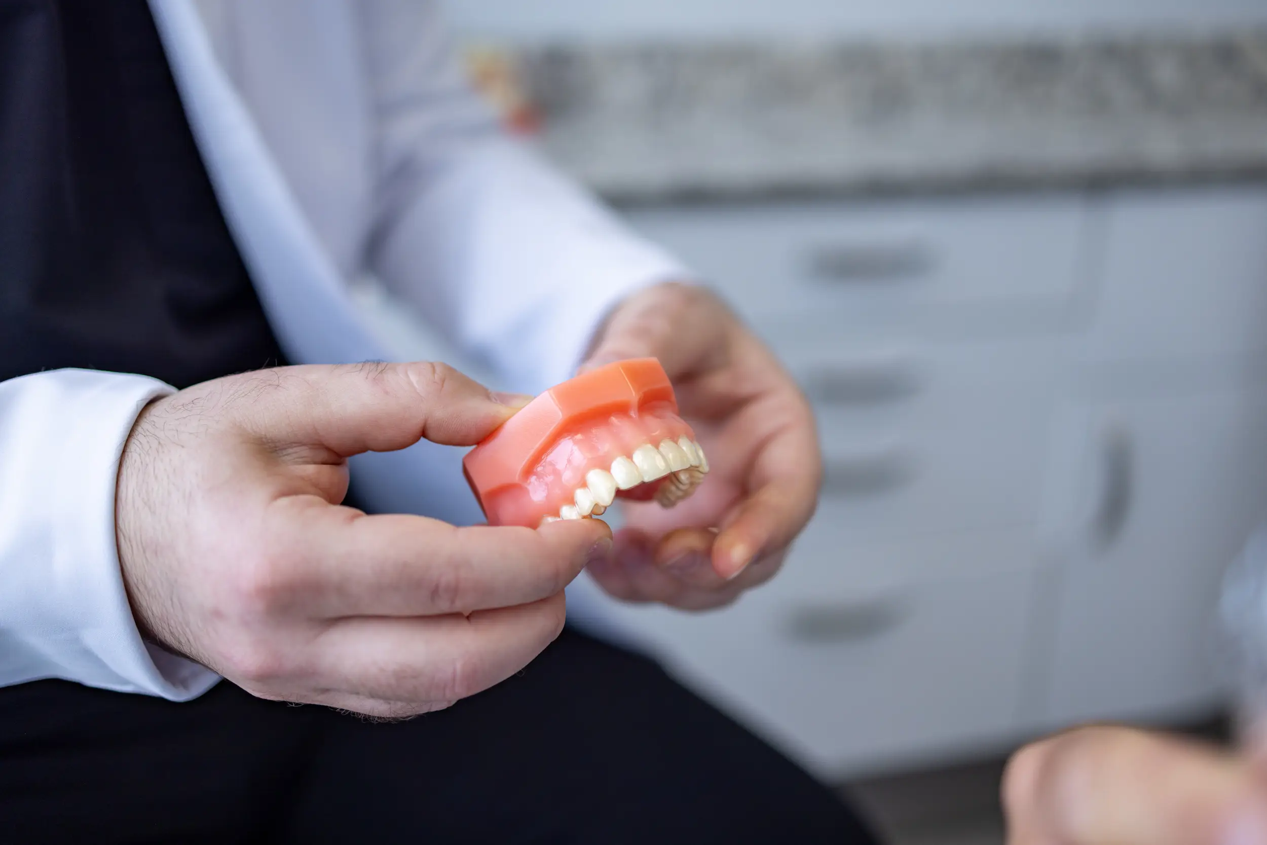 Dentist holding a dental model of upper teeth in a clinical setting.