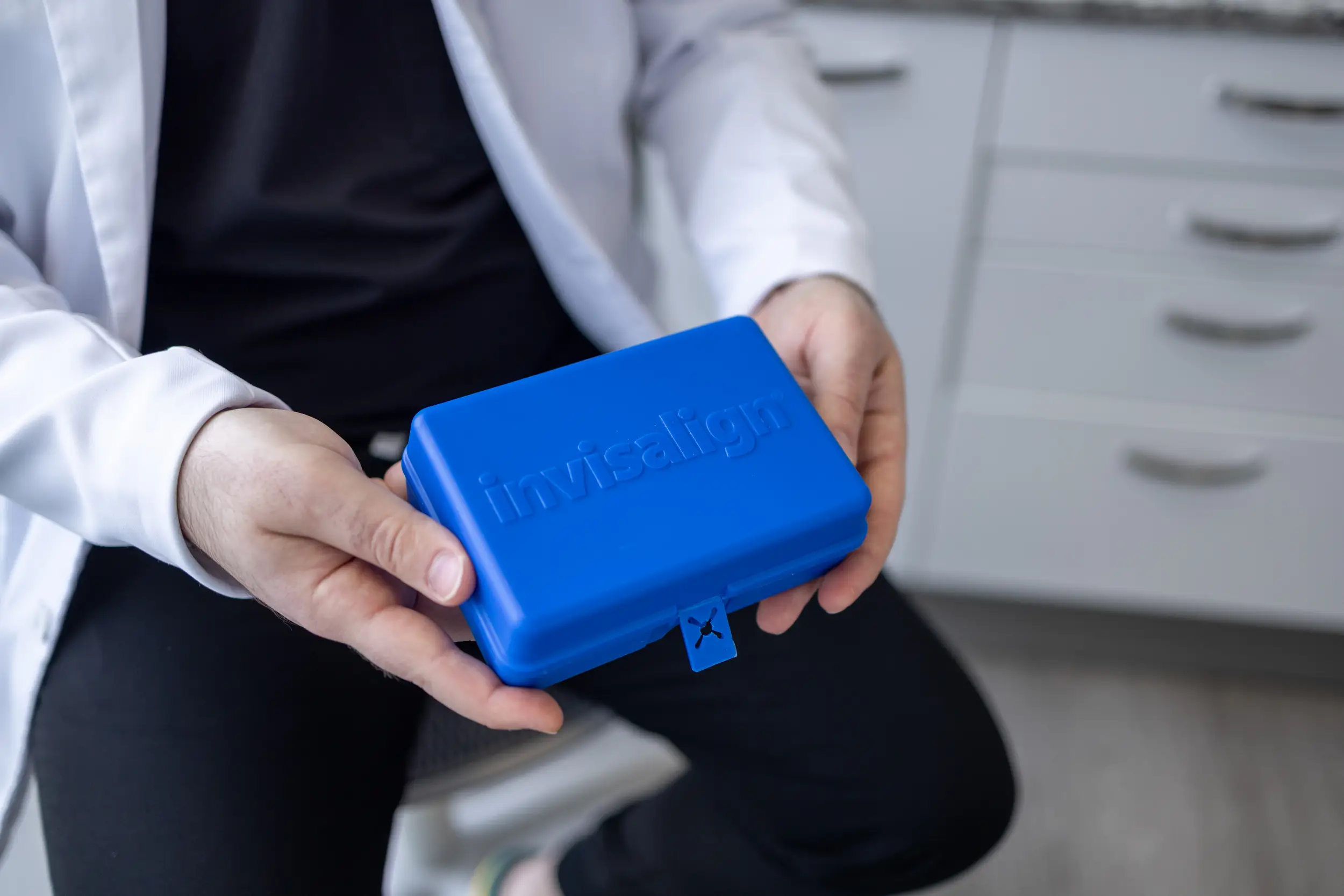 Person in a white coat holding a blue Invisalign case in both hands.
