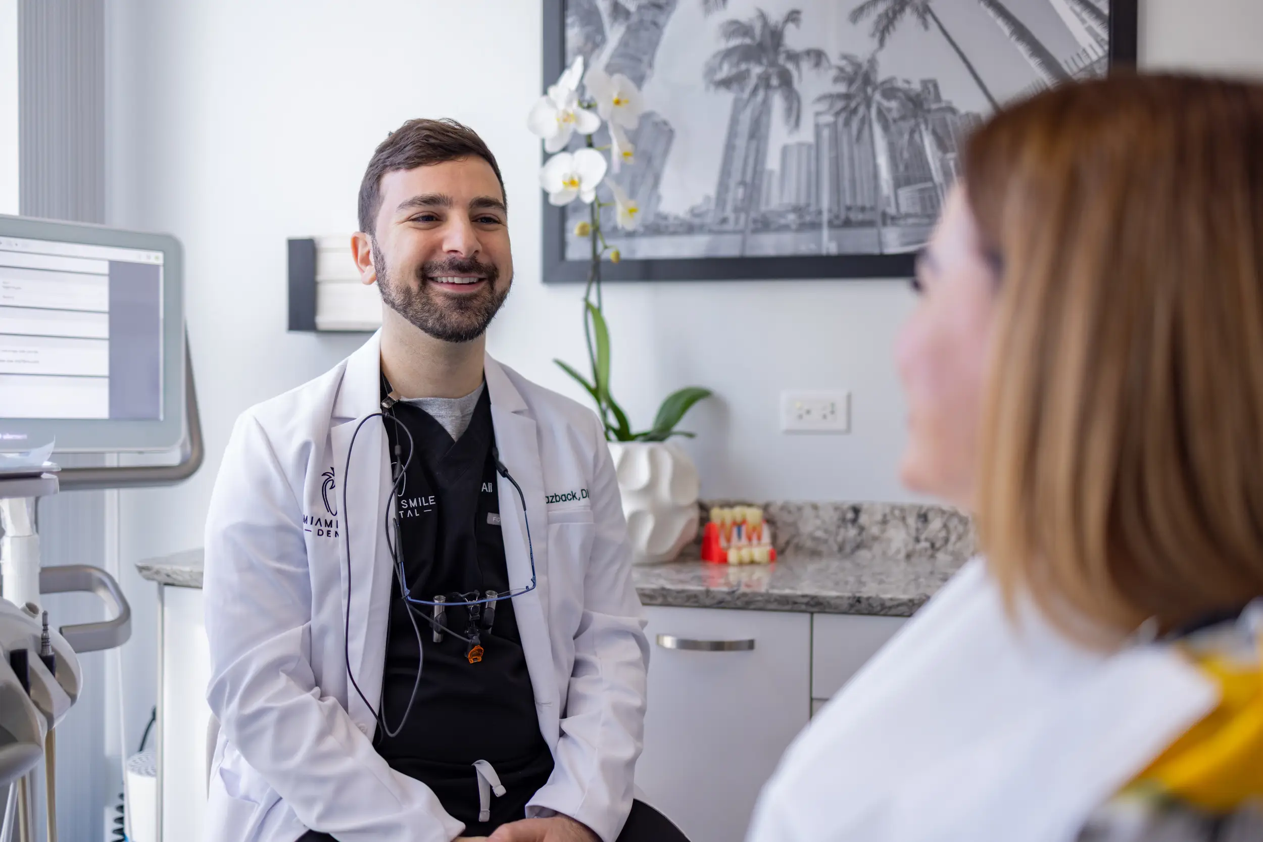 Smiling male dentist in a white coat consulting with a female patient in a dental office.