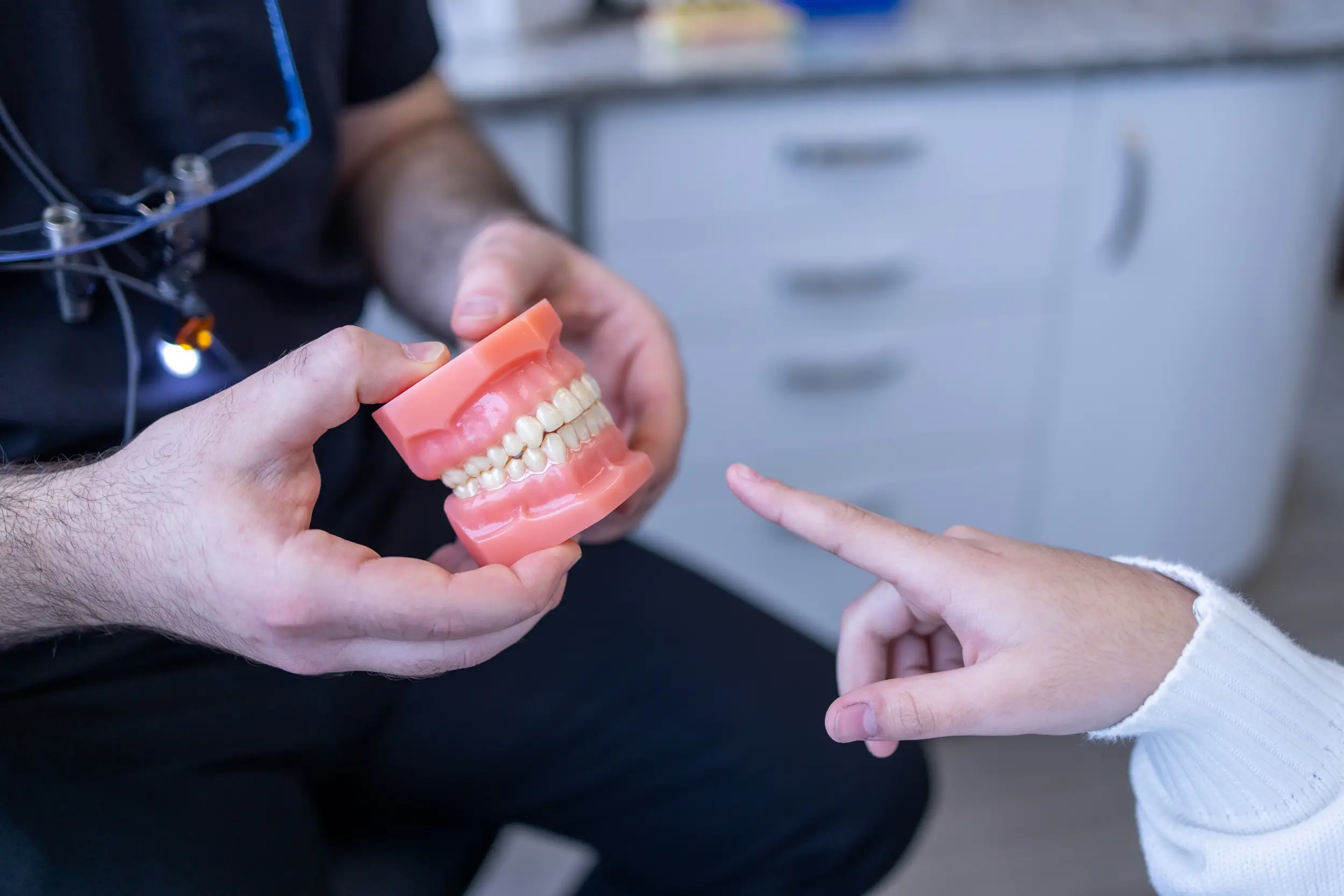 Dental professional holding and showing a model of teeth to a patient pointing at it.