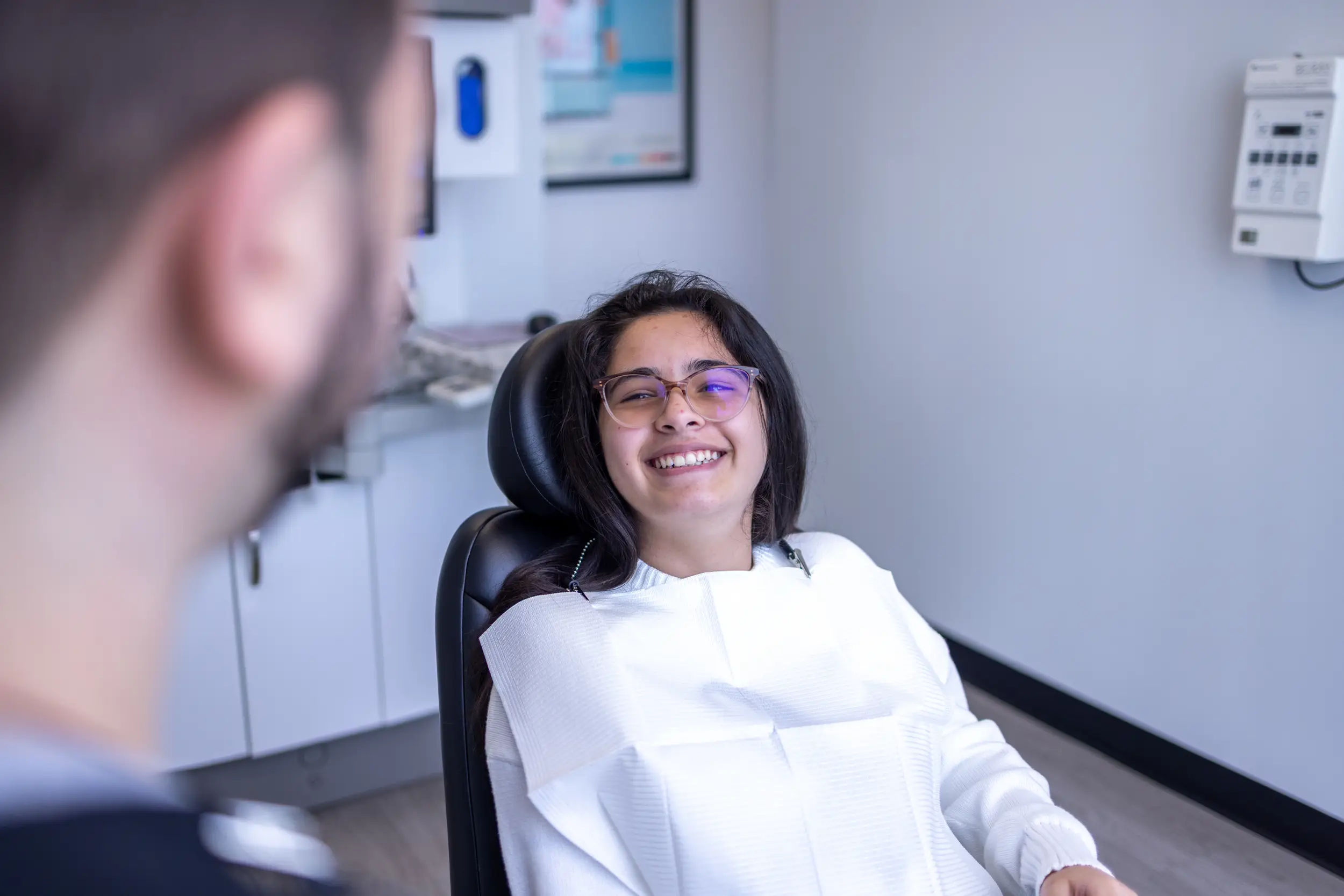 Young woman wearing glasses smiling while seated in a dentist’s chair during a dental visit.