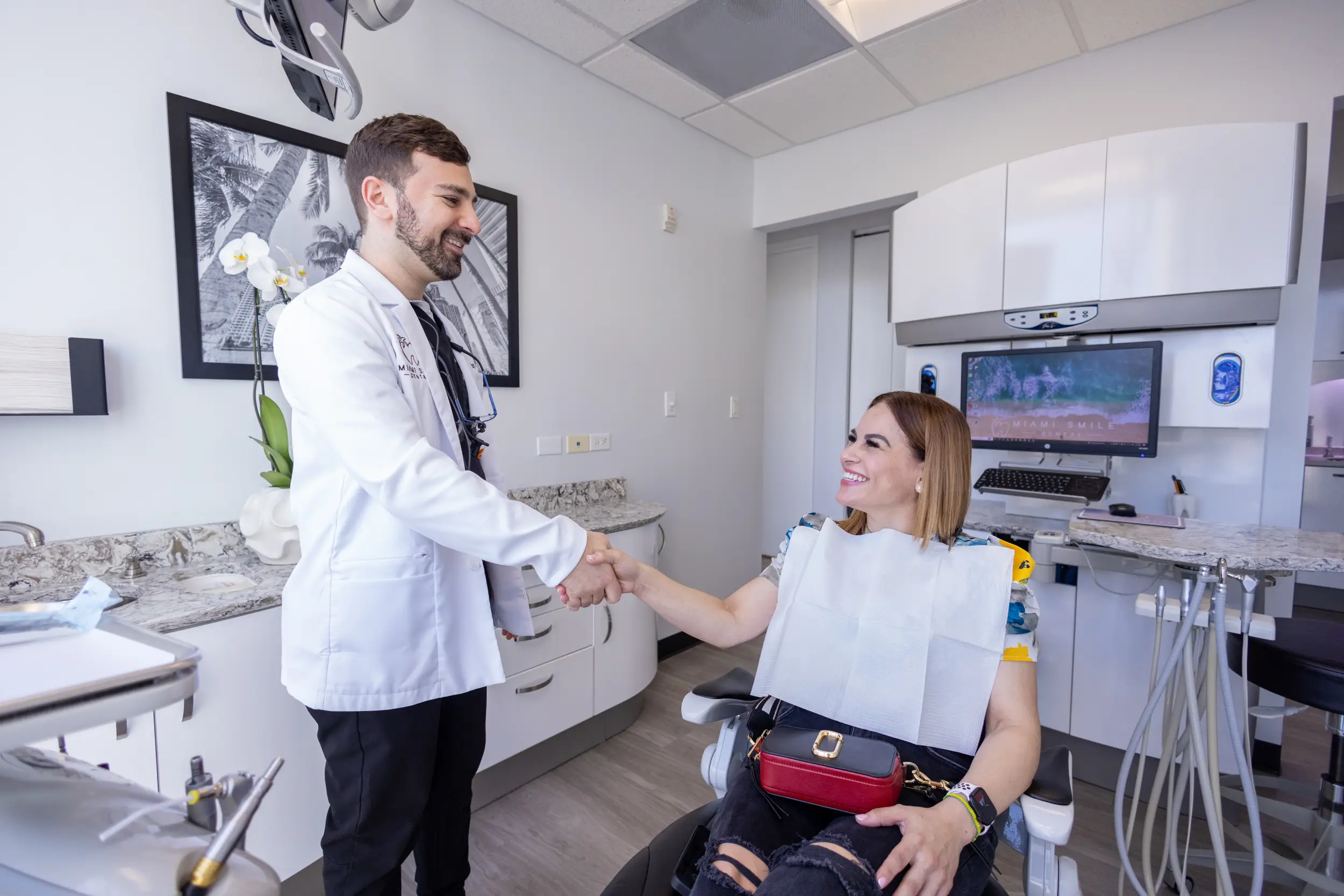Dentist shaking hands with a smiling female patient seated in a dental chair in a modern clinic.