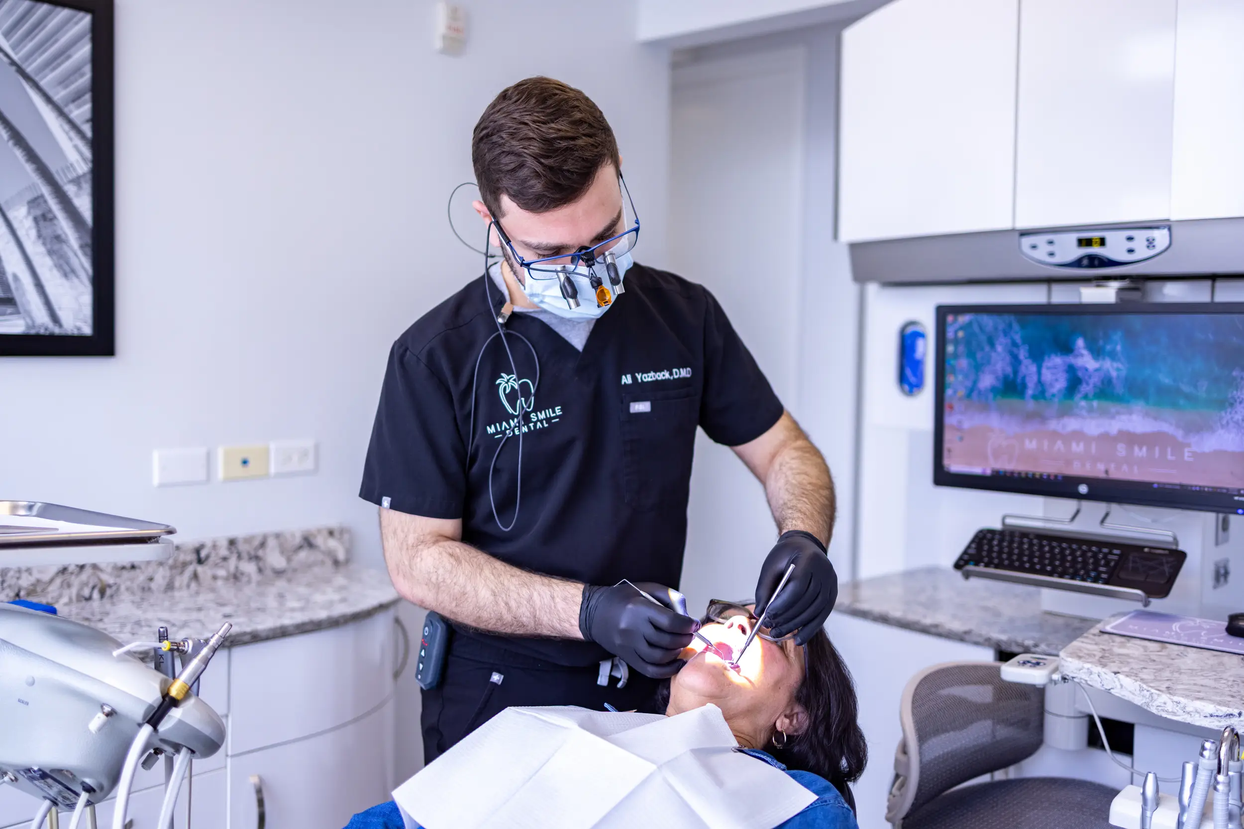 Dentist wearing magnifying glasses and mask examining a patient's teeth in a modern dental office.