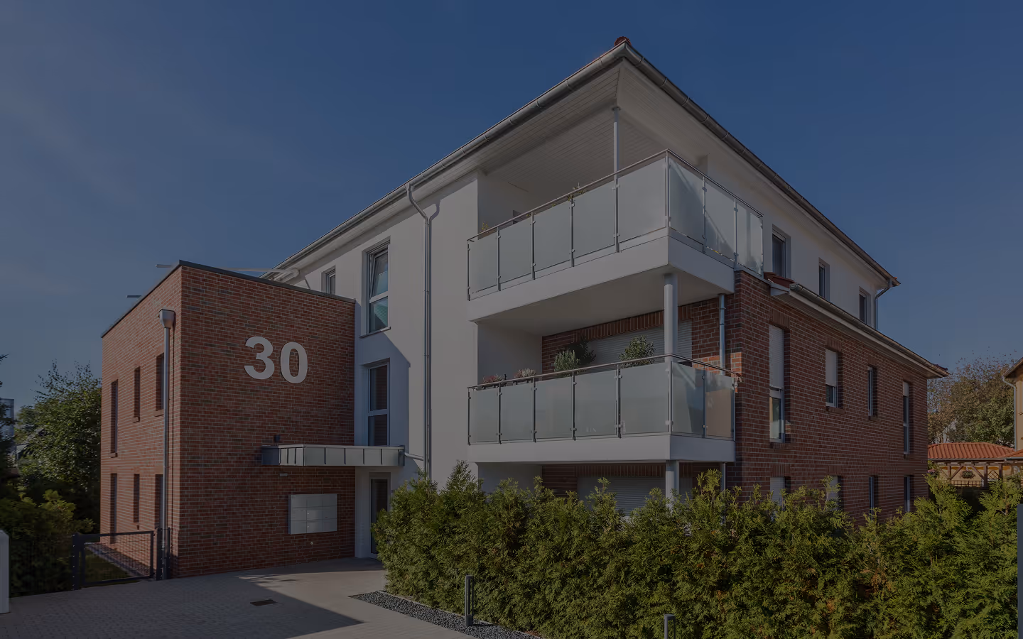 Modernes Mehrfamilienhaus mit roten Ziegeln, zwei Glasbalkonen und großer Nummer 30 an der Fassade.