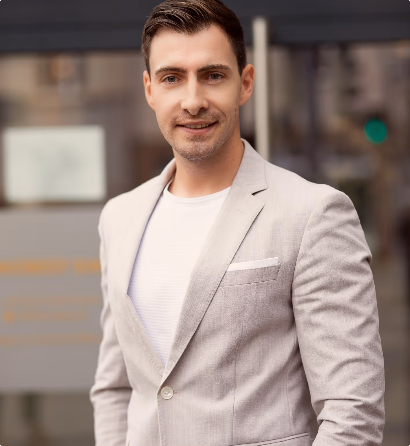 Ein junger Mann in beige Sakko und weißem T-Shirt lächelt in die Kamera.