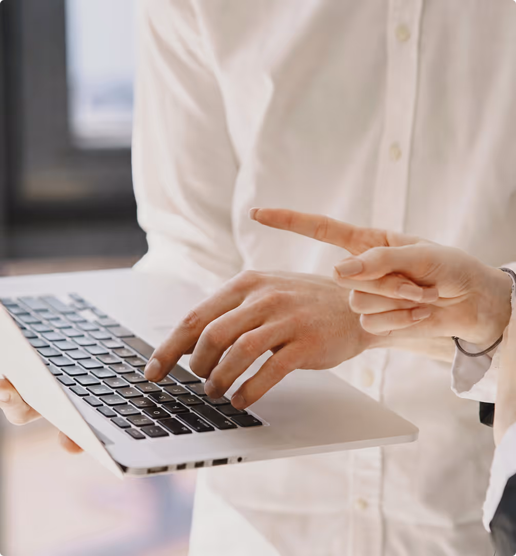 Eine Person tippt auf einer Laptop-Tastatur, während eine andere mit dem Finger auf den Bildschirm zeigt.