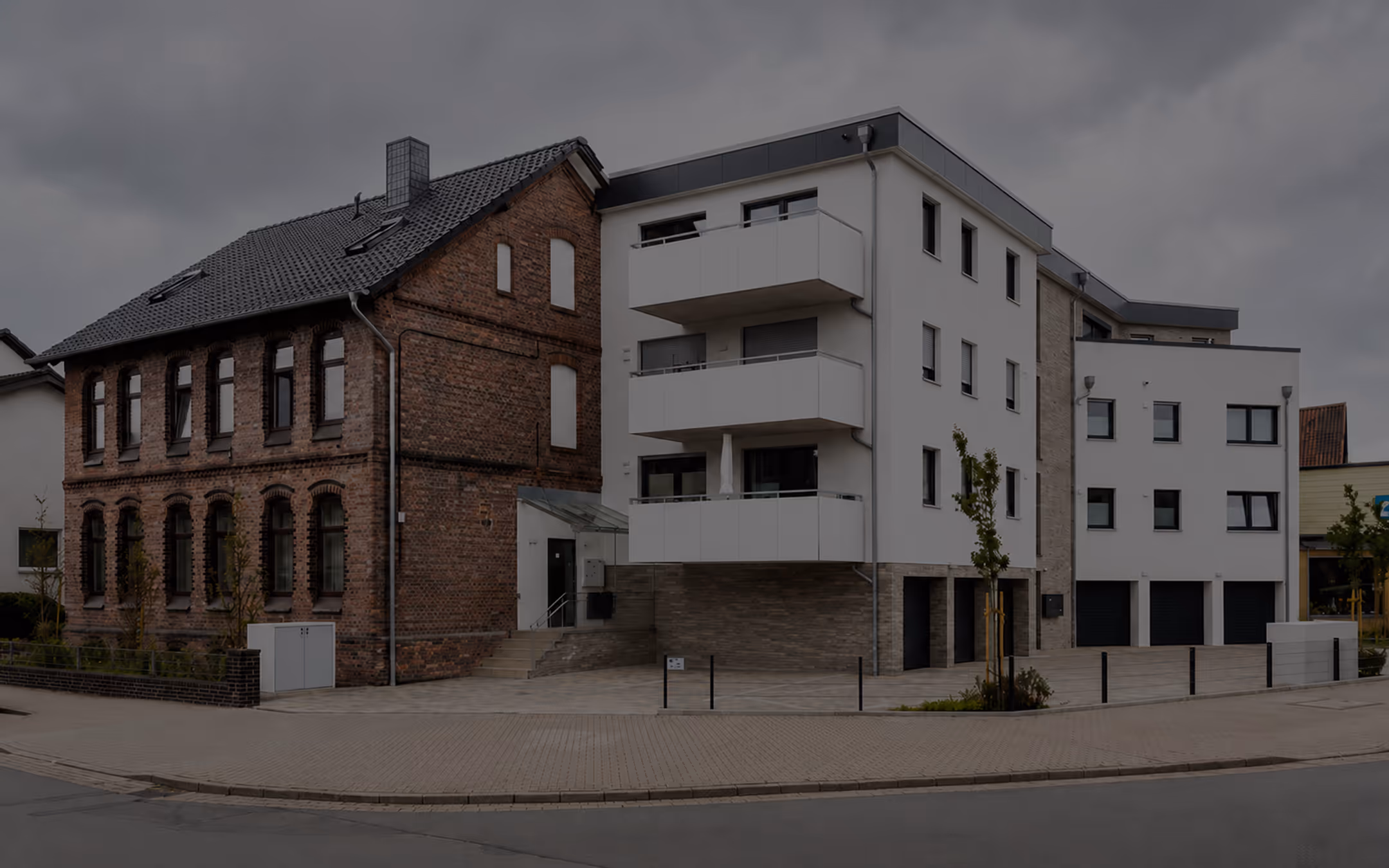 Ein modernes Mehrfamilienhaus mit weißen Balkonen neben einem alten ziegelsteingebäude bei bewölktem Himmel.