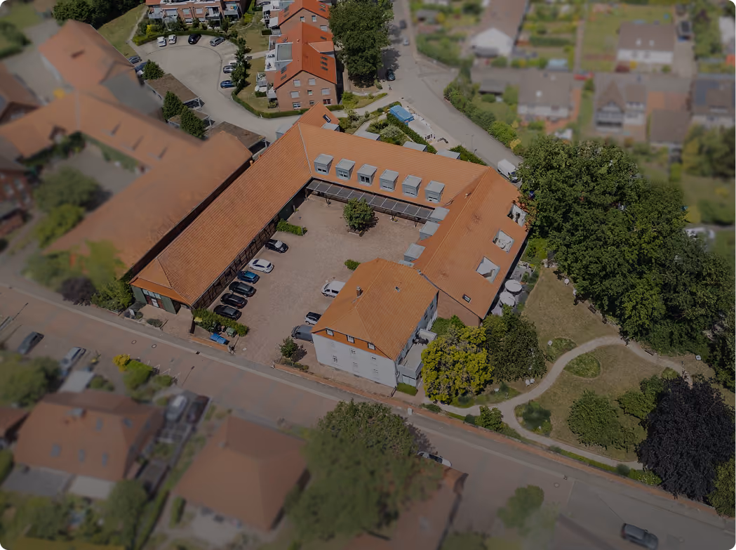 Luftaufnahme eines U-förmigen Gebäudes mit rotem Dach und Parkplätzen im Innenhof.