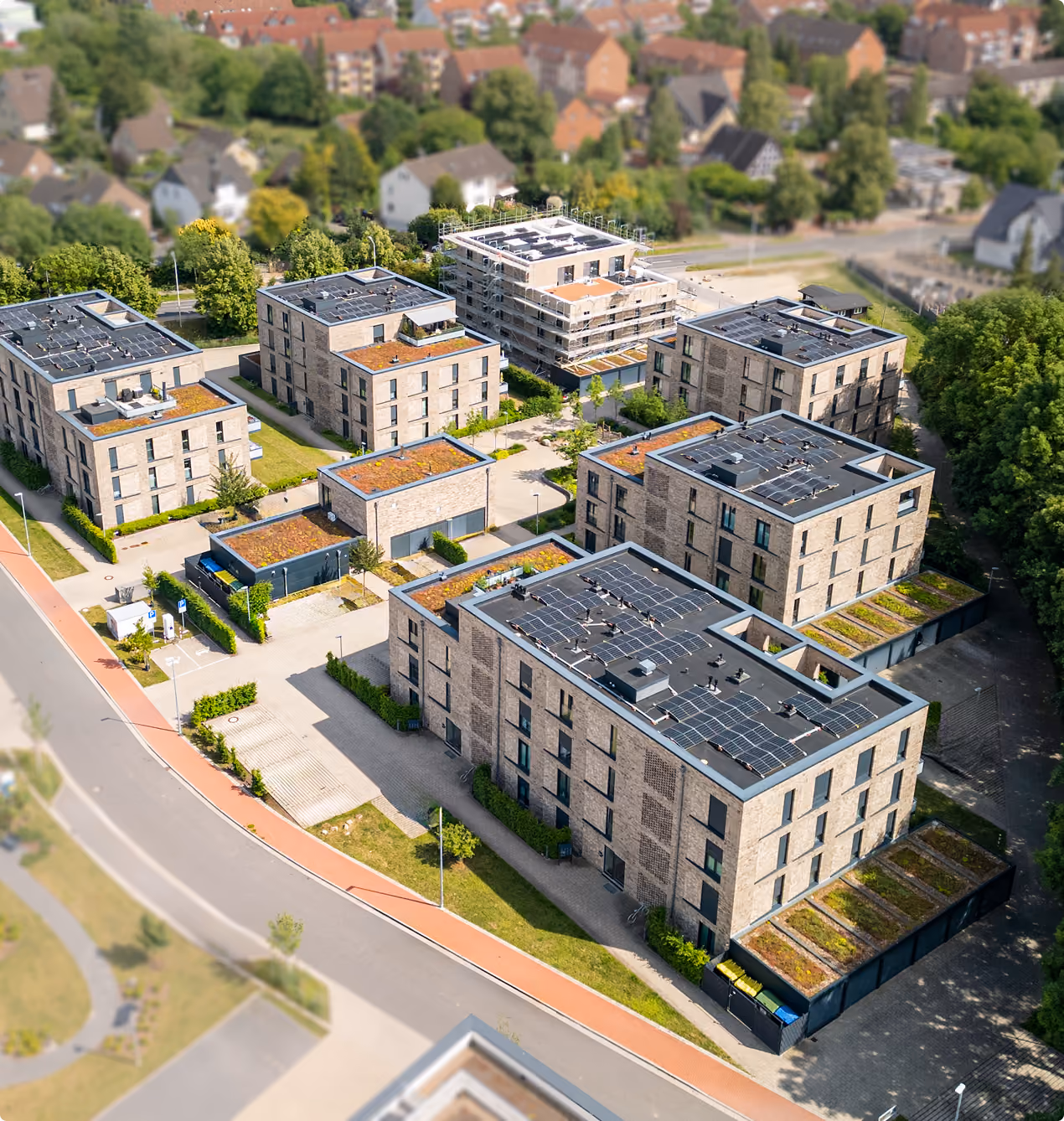Luftaufnahme moderner Wohngebäude mit Solarpanelen und begrünten Dächern in einer Wohnsiedlung.