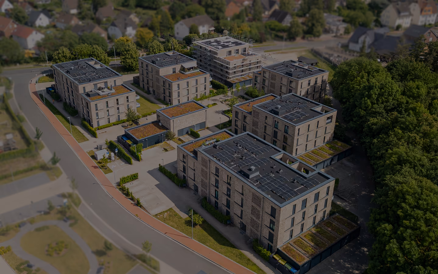 Luftaufnahme eines modernen Wohnkomplexes mit mehreren Gebäuden, Solarzellen und viel Grün.