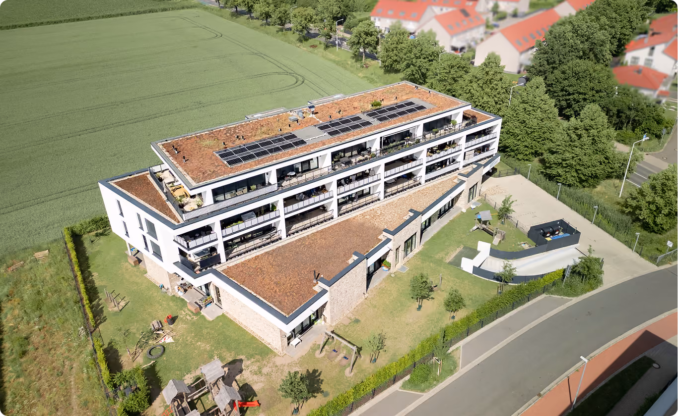 Luftaufnahme eines modernen Wohngebäudes mit Solarpanelen auf dem Dach und einem Spielplatz im Garten.