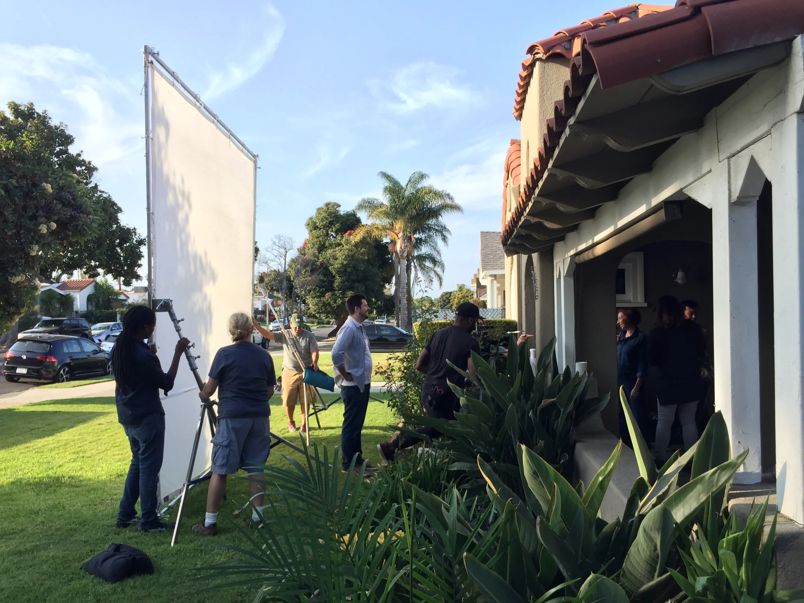 Production crew and lighting equipment filming outside a house on location.