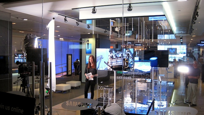 Video production setup with a presenter, camera crew and lighting in an electronics showroom.