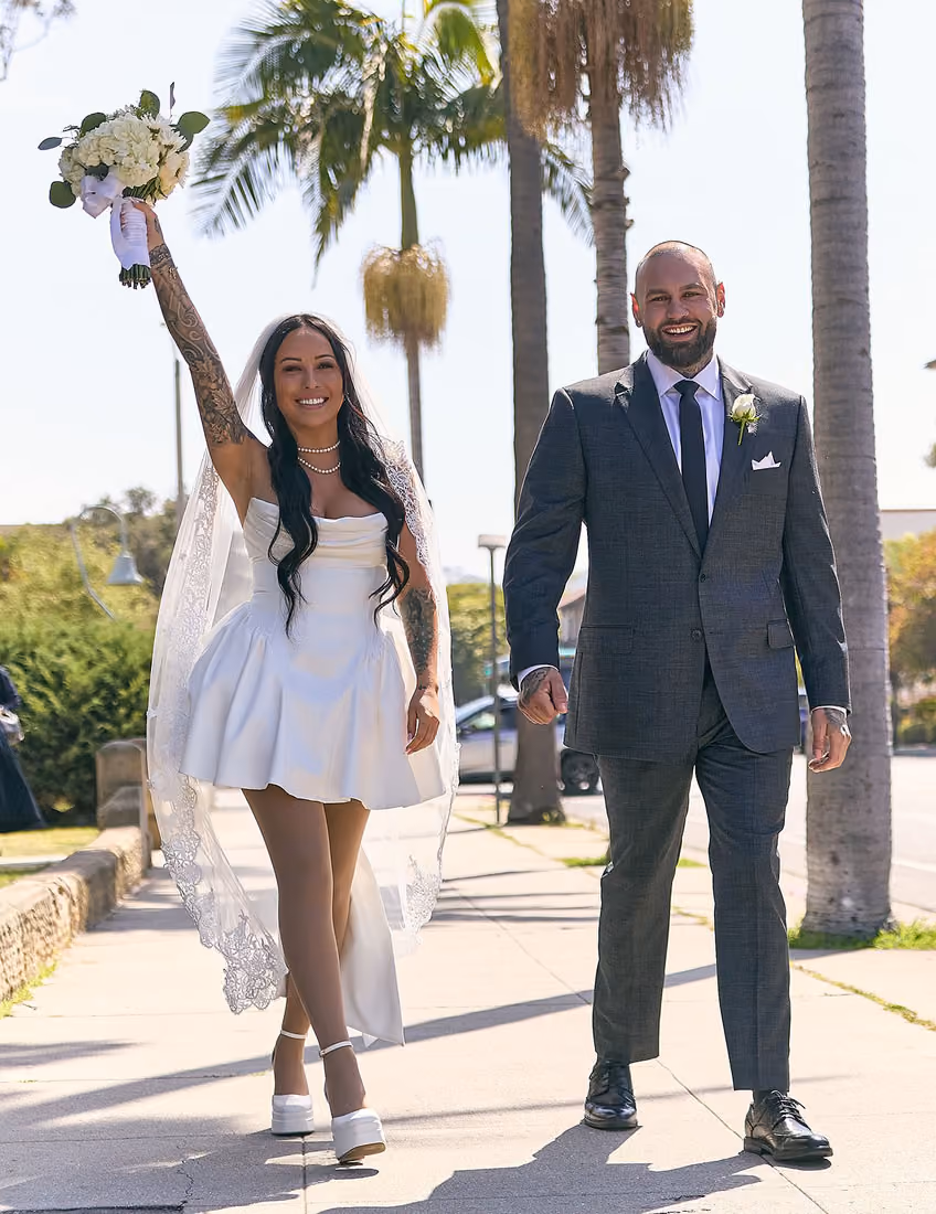Offbeat bride and groom in victory pose with bouquet.