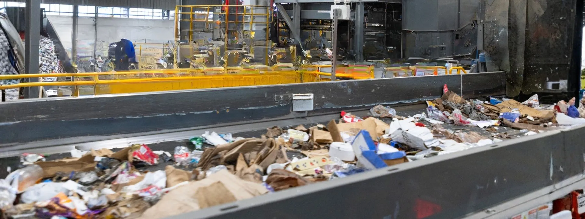 Conveyor belt carrying mixed recyclable materials like cardboard, paper, plastic, and aluminum cans.