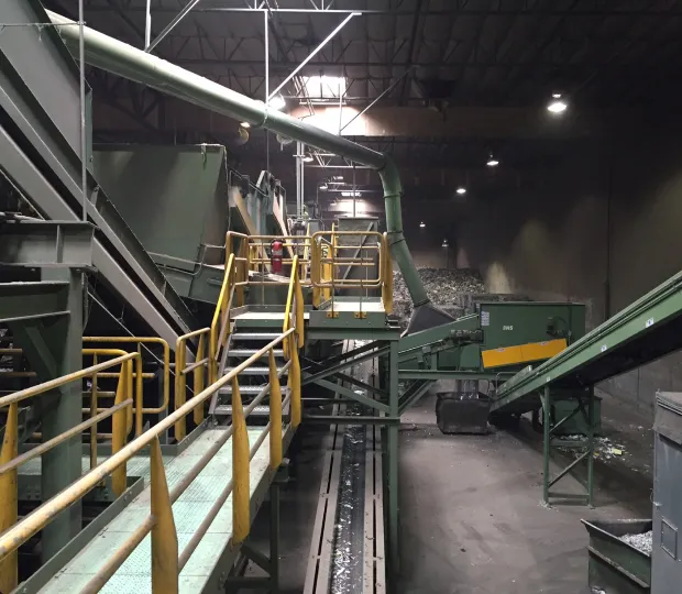 Industrial recycling facility with conveyor belts and yellow railings under metal roof lighting.