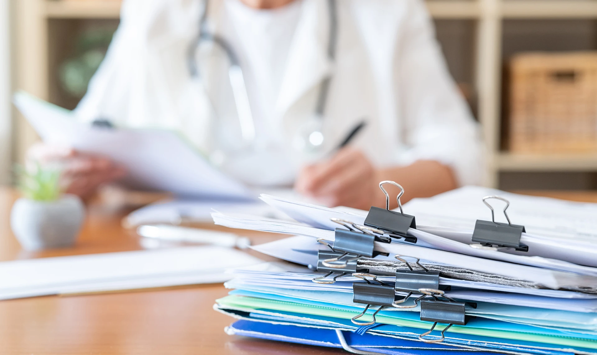 Healthcare professional reviewing a large stack of medical records and documents at a desk.