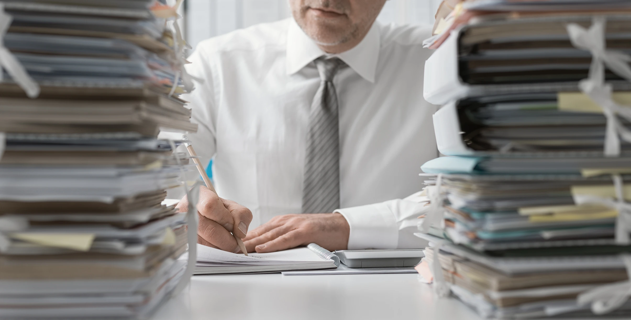 Administrative professional working through large stacks of records and paperwork at a desk.