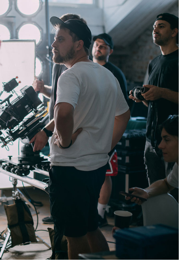 Film crew members stand around professional camera equipment in a studio setting with bright lights.