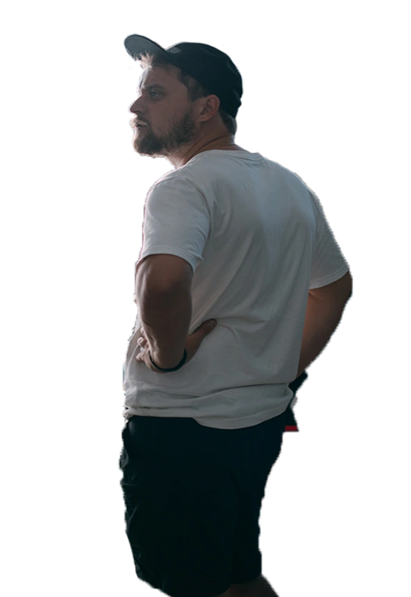 Man with beard in white t-shirt and black shorts standing with hands on hips looking to the left.