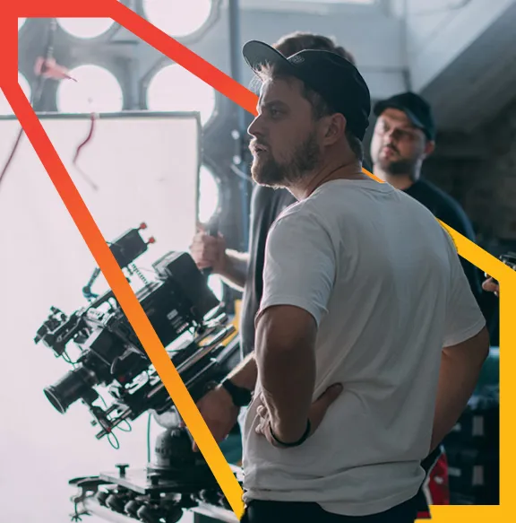 Film crew members working with a camera and lighting equipment inside a dimly lit studio.