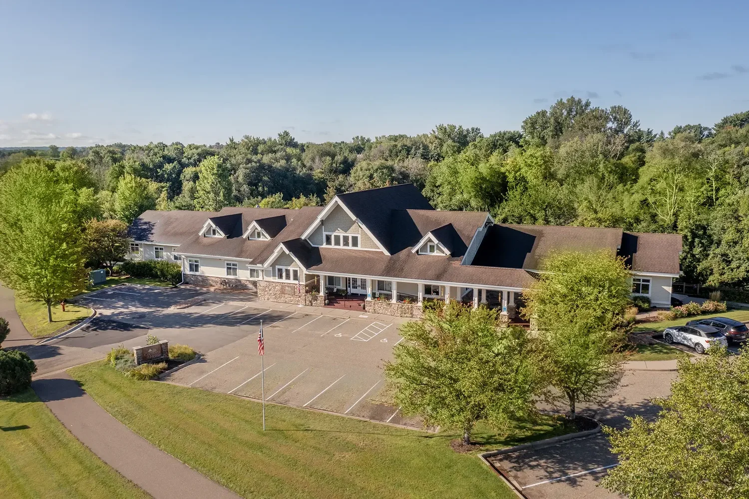 Large house with brown roof surrounded by trees and parking lots on a sunny day.