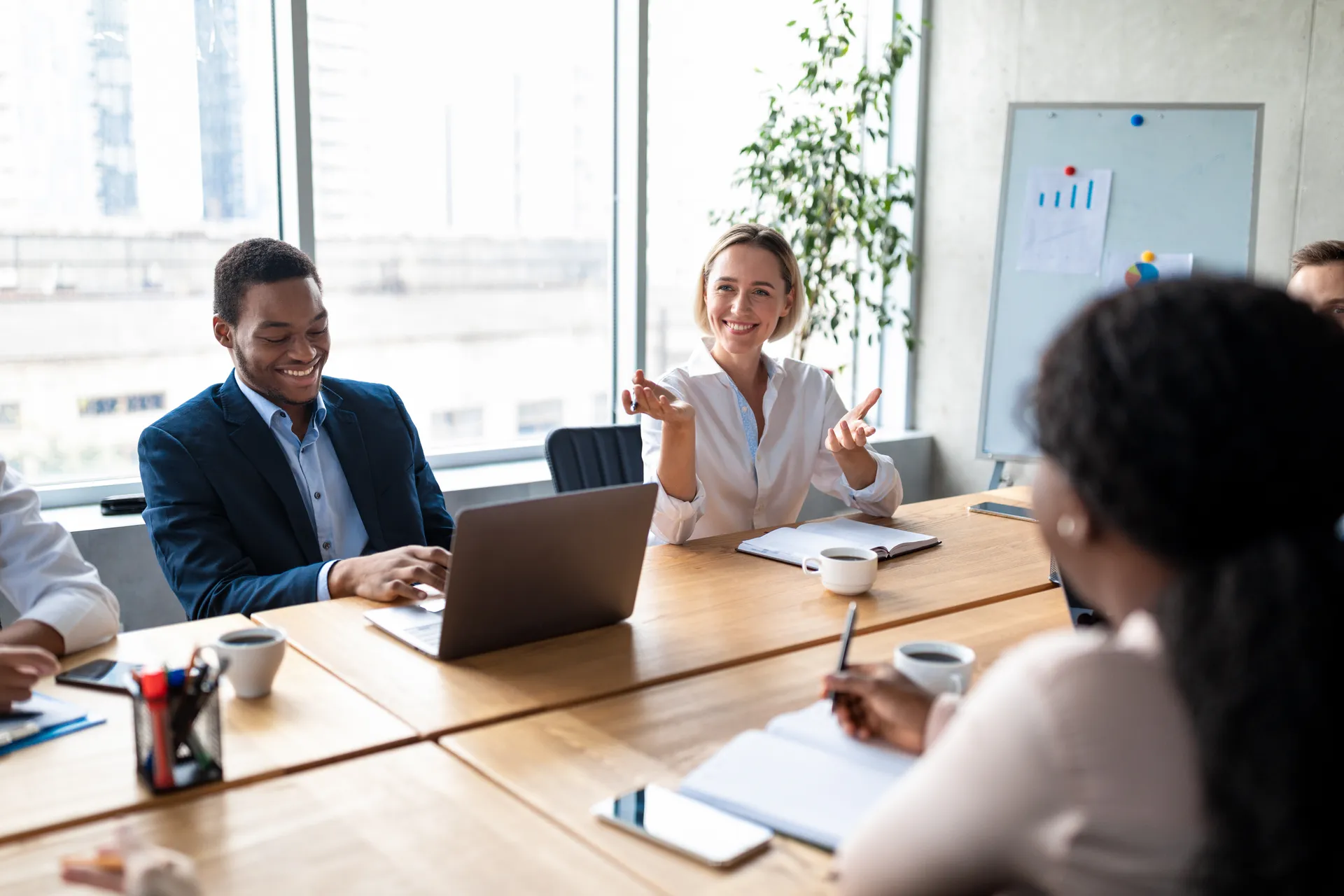Smiling coworkers engaged in a meeting around a wooden conference table with notebooks and coffee cups.