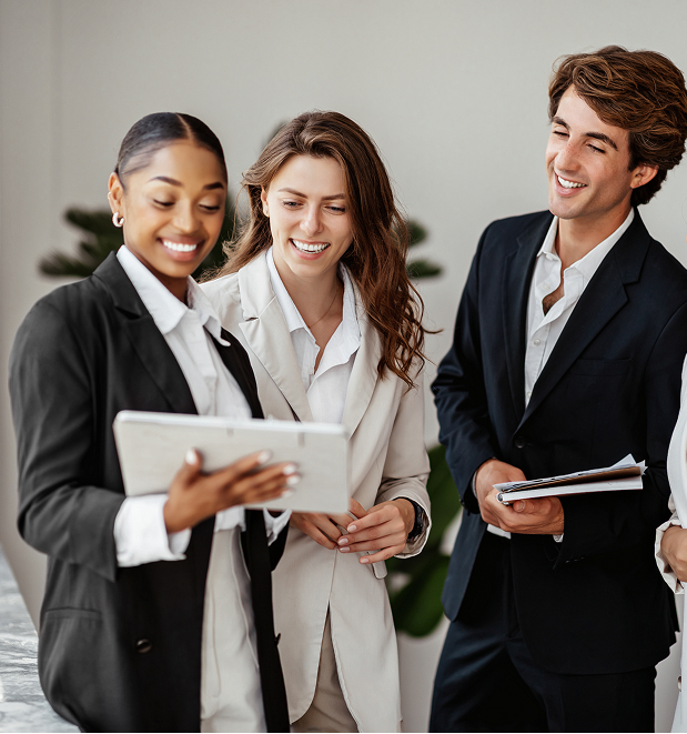Three young professionals smiling and looking at a tablet during a business meeting.