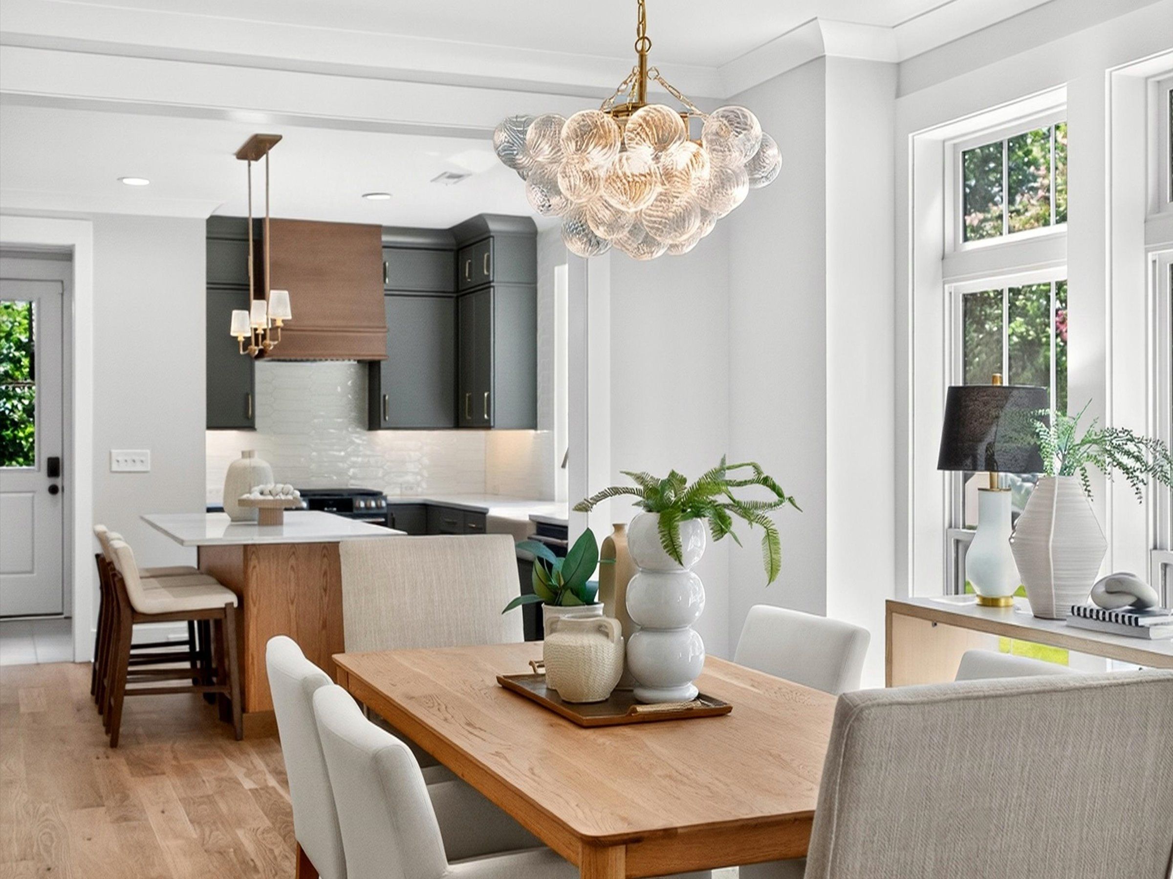 Dining area with a wood table and a glass bubble chandelier, open to a kitchen with dark gray cabinets and a wood-trimmed island