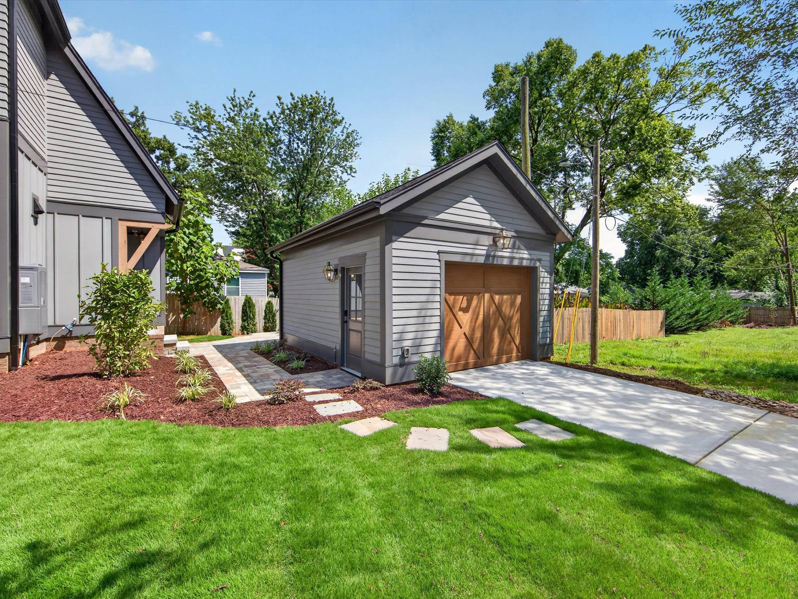 Detached gray garage with a wood carriage door, a stepping-stone path, and a fresh lawn