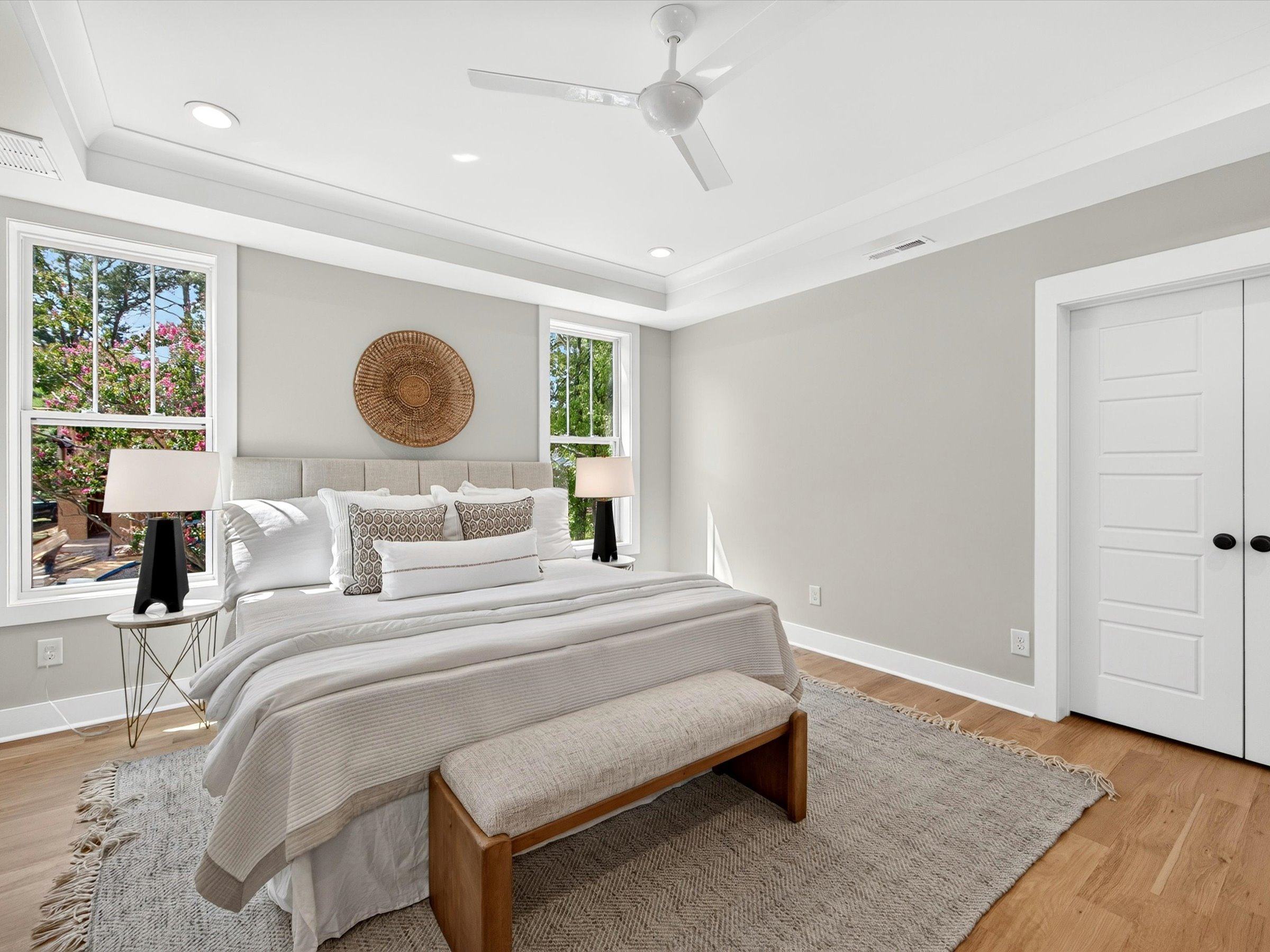 Primary bedroom with a tray ceiling, ceiling fan, two windows, and light oak floors