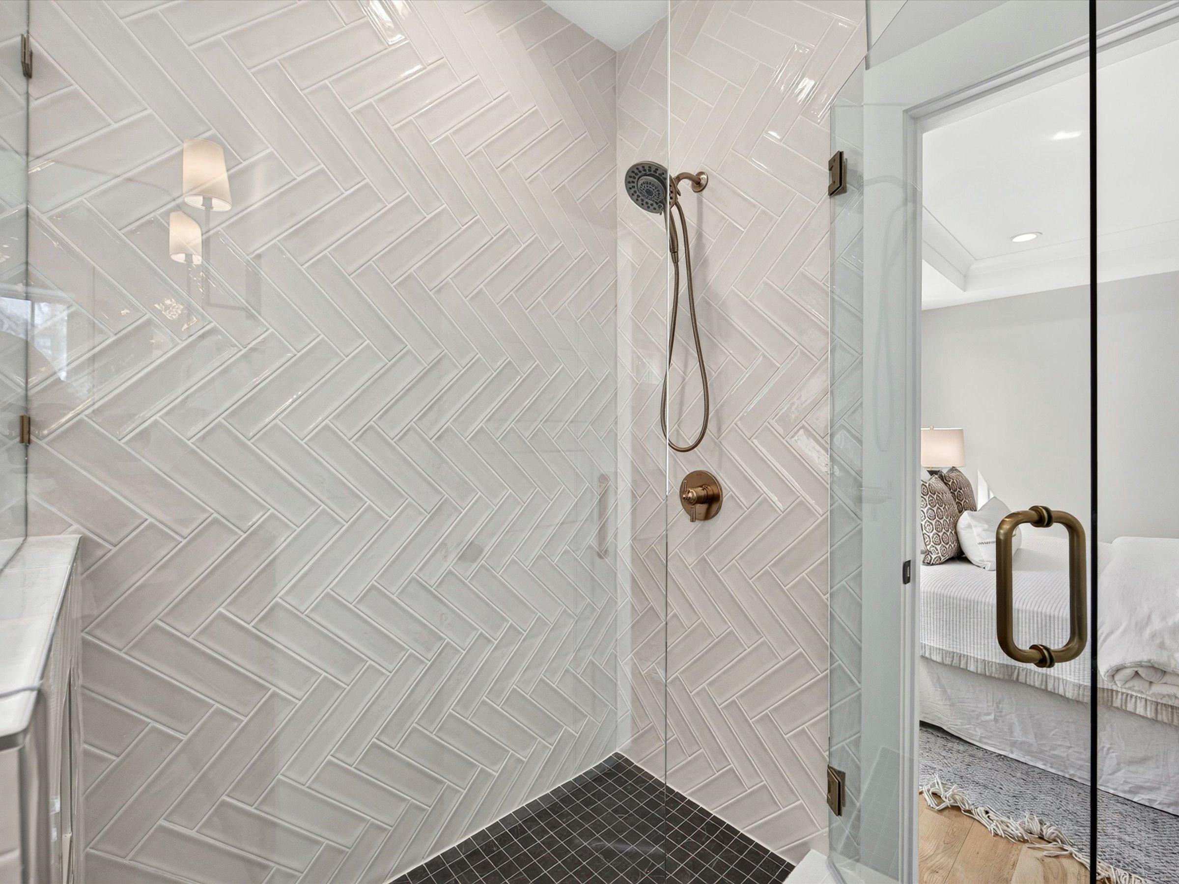 Walk-in shower with white herringbone tile, a brass handheld shower, and a frameless glass door