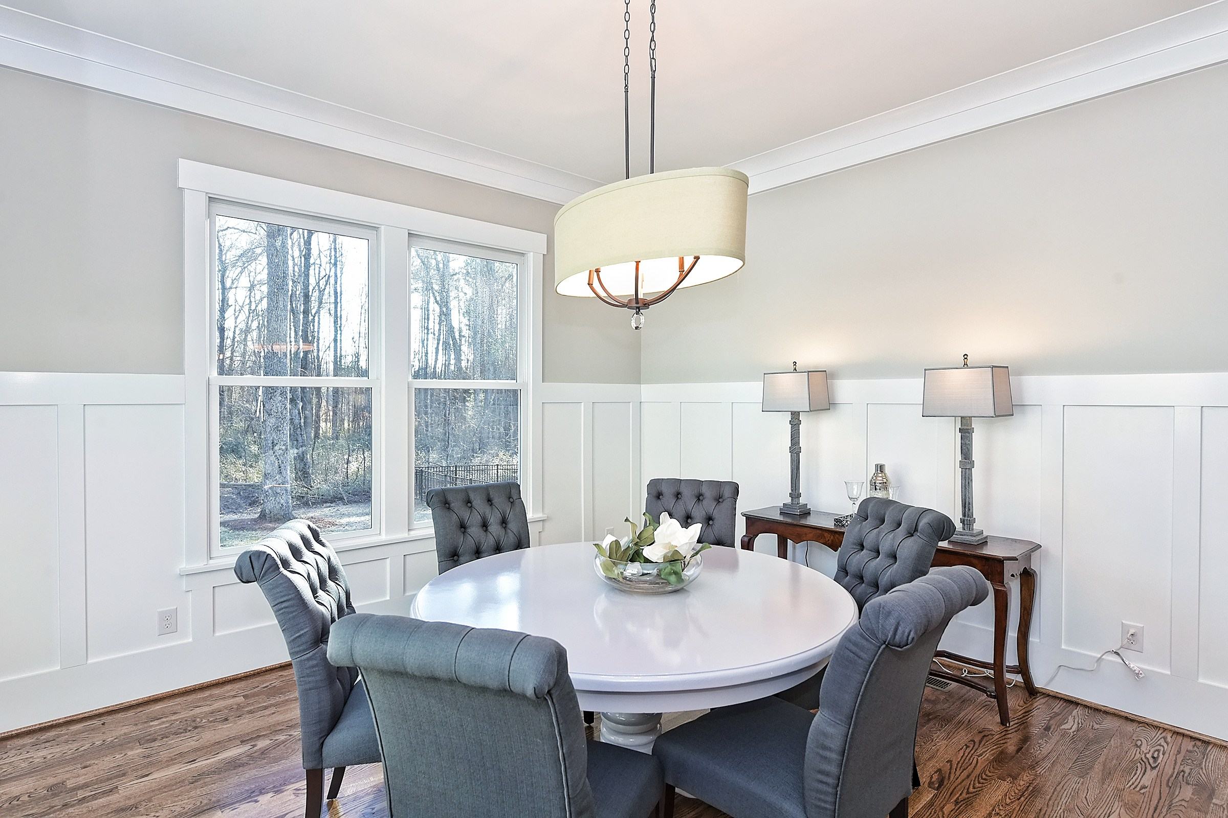 Dining room with wainscoting, a round white table with upholstered chairs, and a drum pendant light