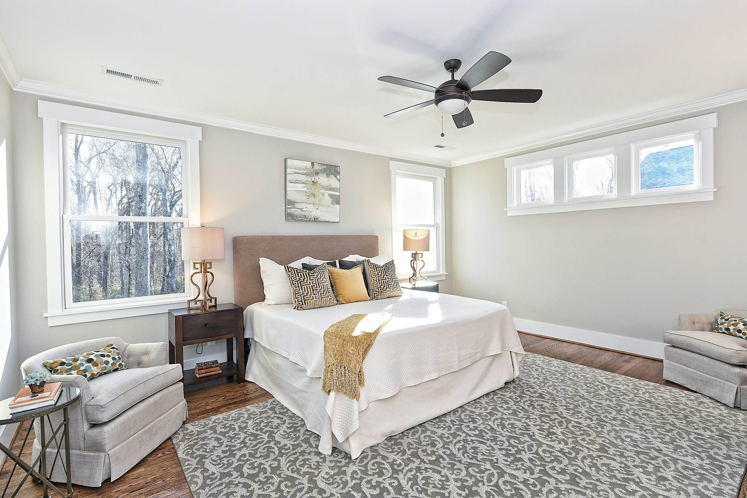 Bedroom with a ceiling fan, a large window, a patterned rug, and a reading chair